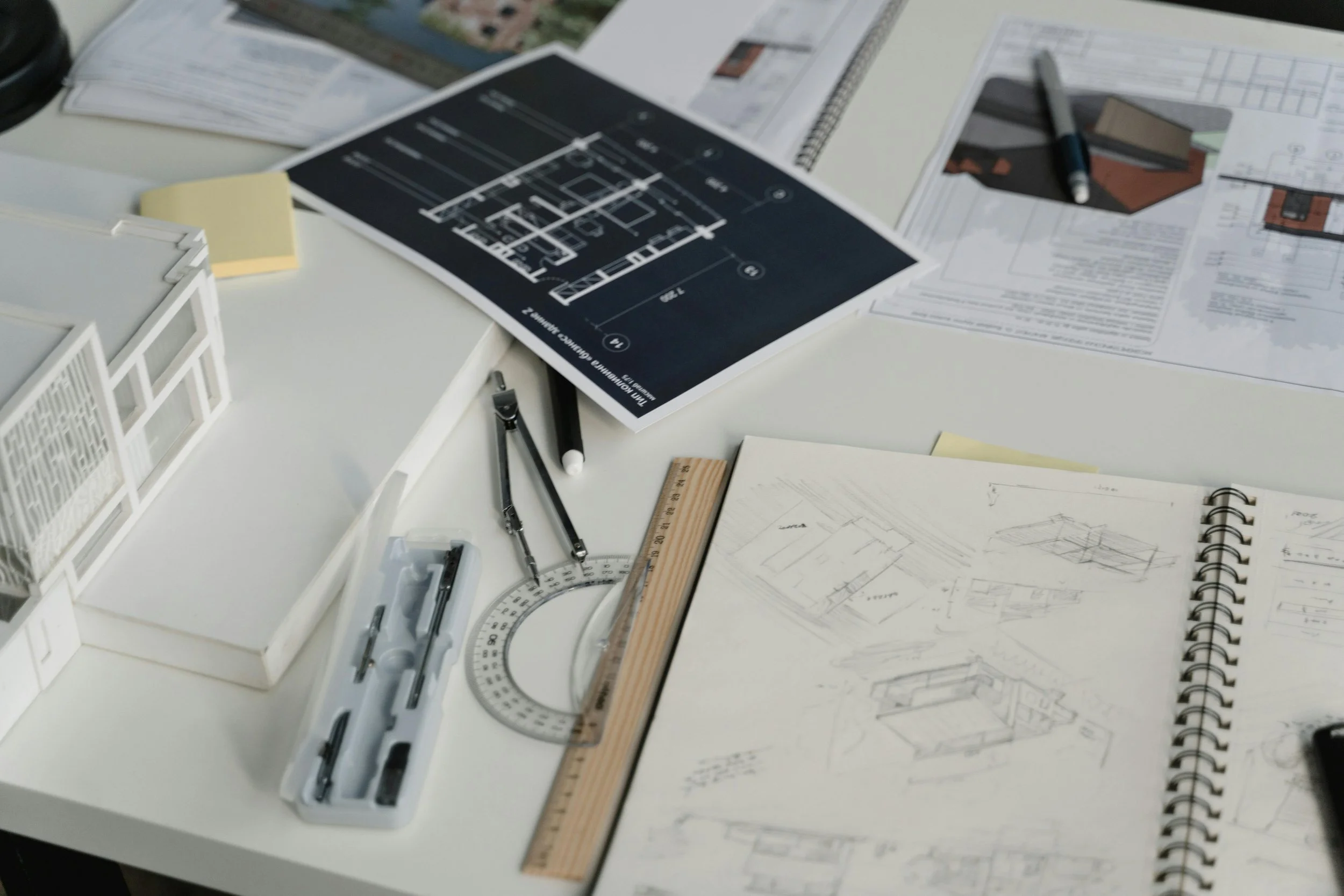 Architectural drawings, sketches, drafting tools, and modeling materials on a desk, indicating a workspace for architectural design.