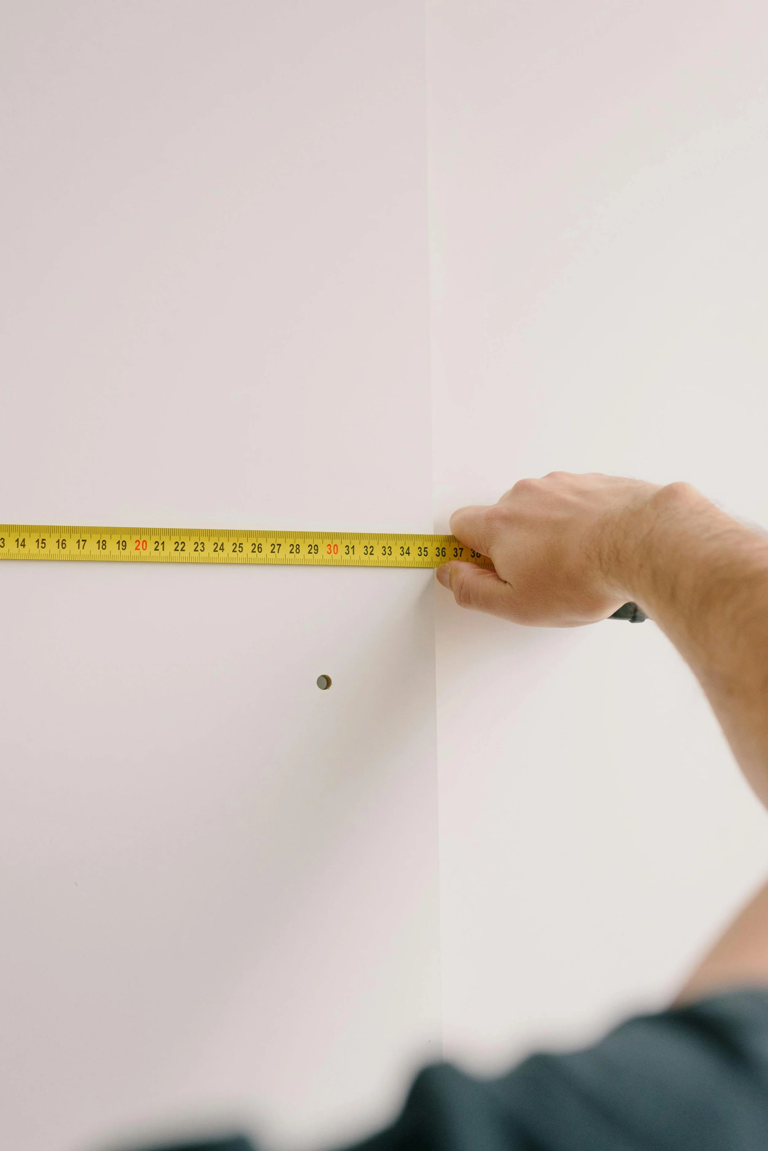 A person measuring a wall with a yellow tape measure, showing approximately 37 inches.