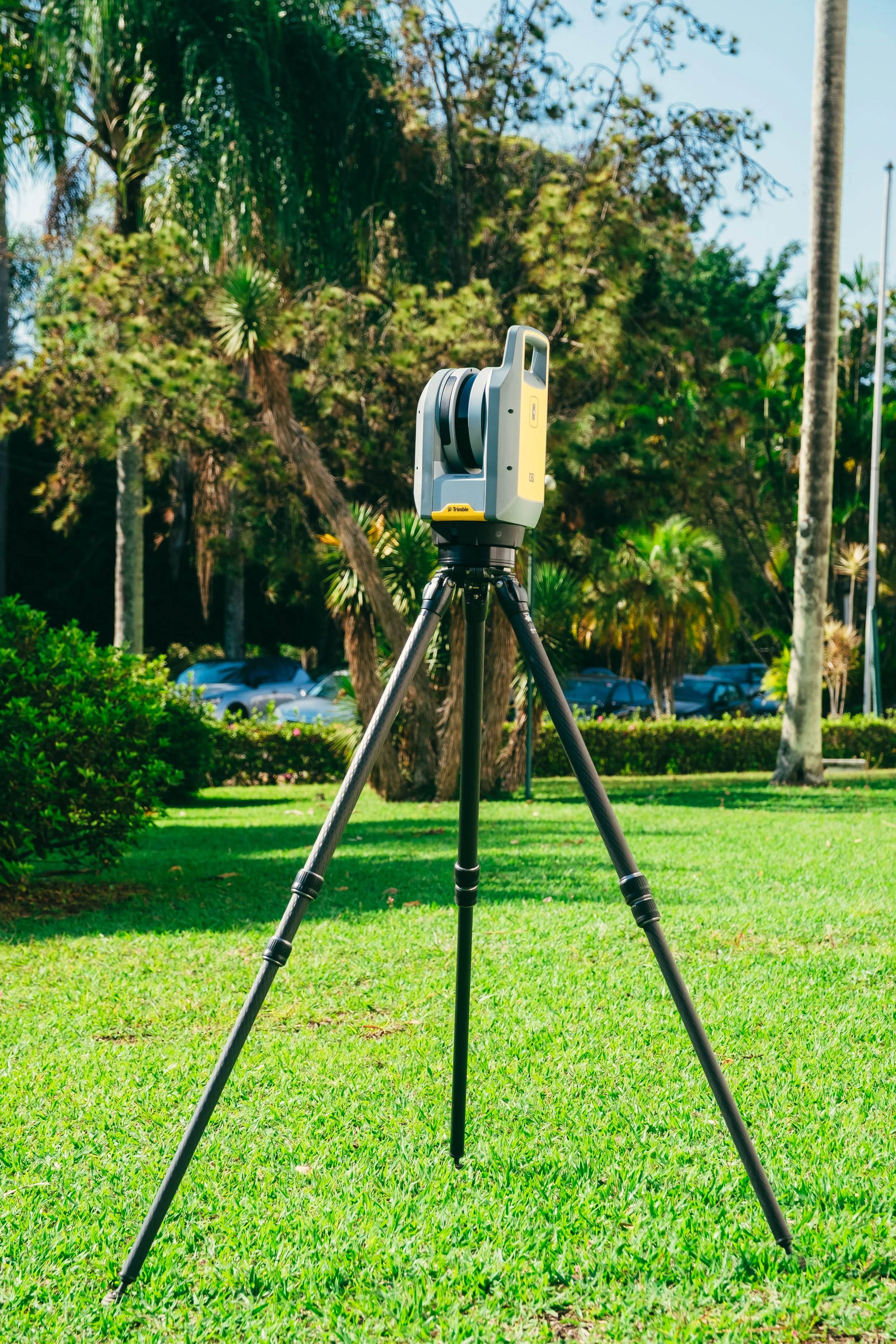 Equipamento de levantamento topográfico montado em tripé, em um espaço ao ar livre com árvores e grama