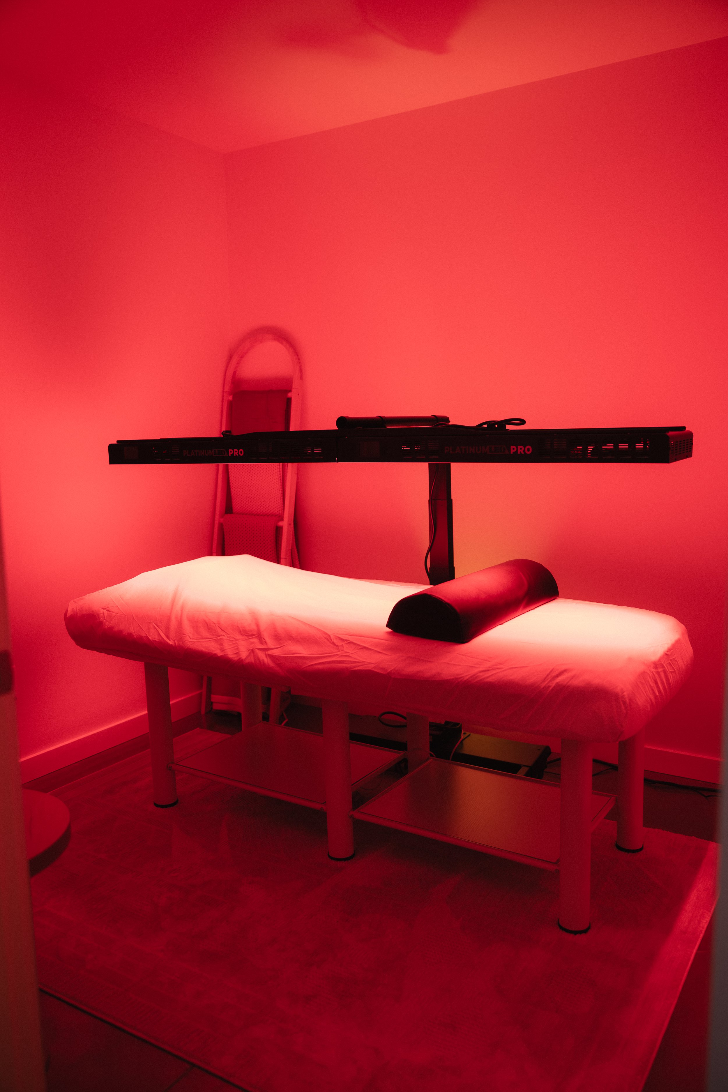 A massage table in a room bathed in red light, with a pillow at the head of the table and an adjustable armrest. A mirror is visible on the wall behind the table.