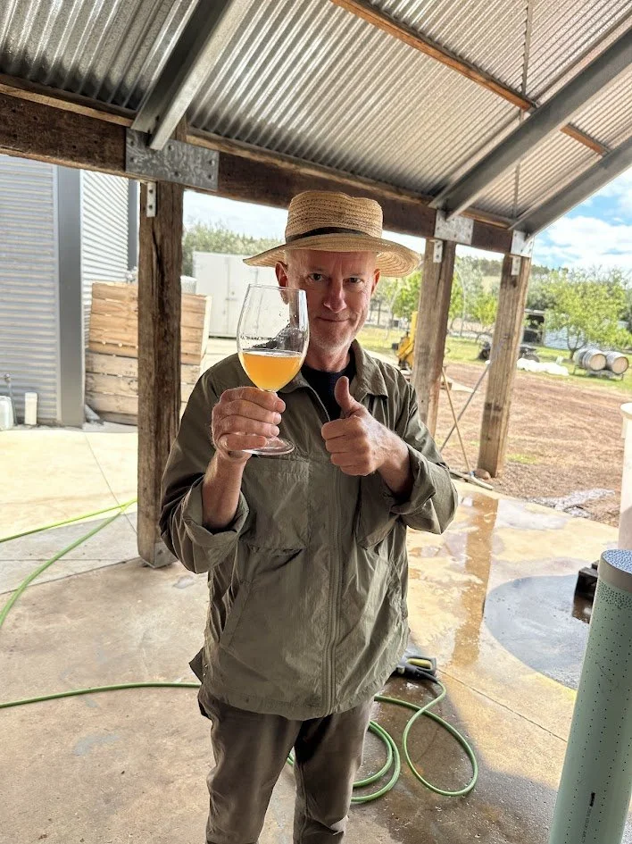 Scott Ireland, winegrower during vintage 2025 holding a glass of Chardonnay juice. Even though he loves Pinot Noir he still gives a thumbs-up.