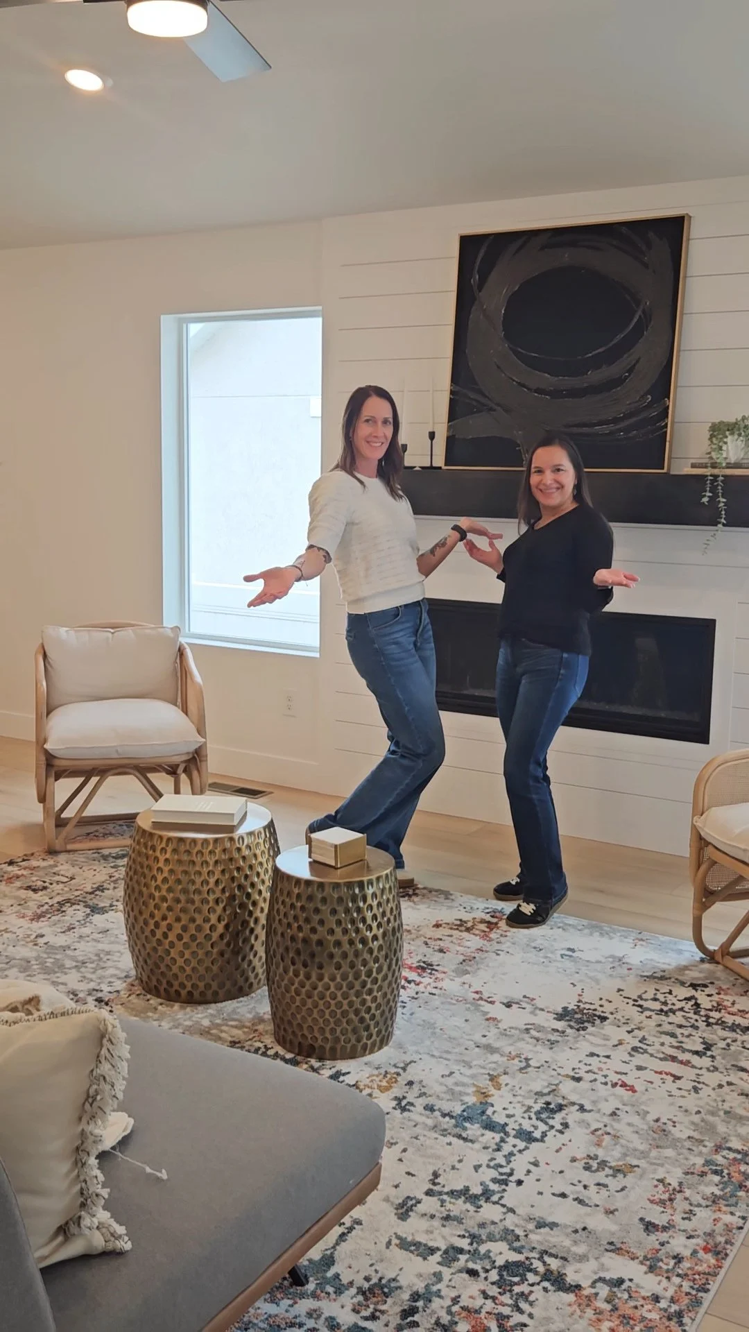 Two women dancing in a living room with a fireplace and abstract art above it.