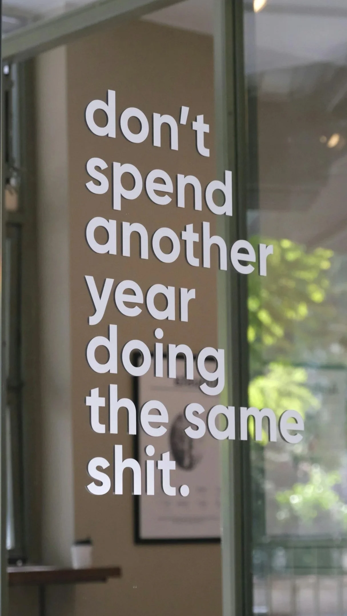 Texto en una ventana que dice: "don't spend another year doing the same shit" en letras blancas grandes.