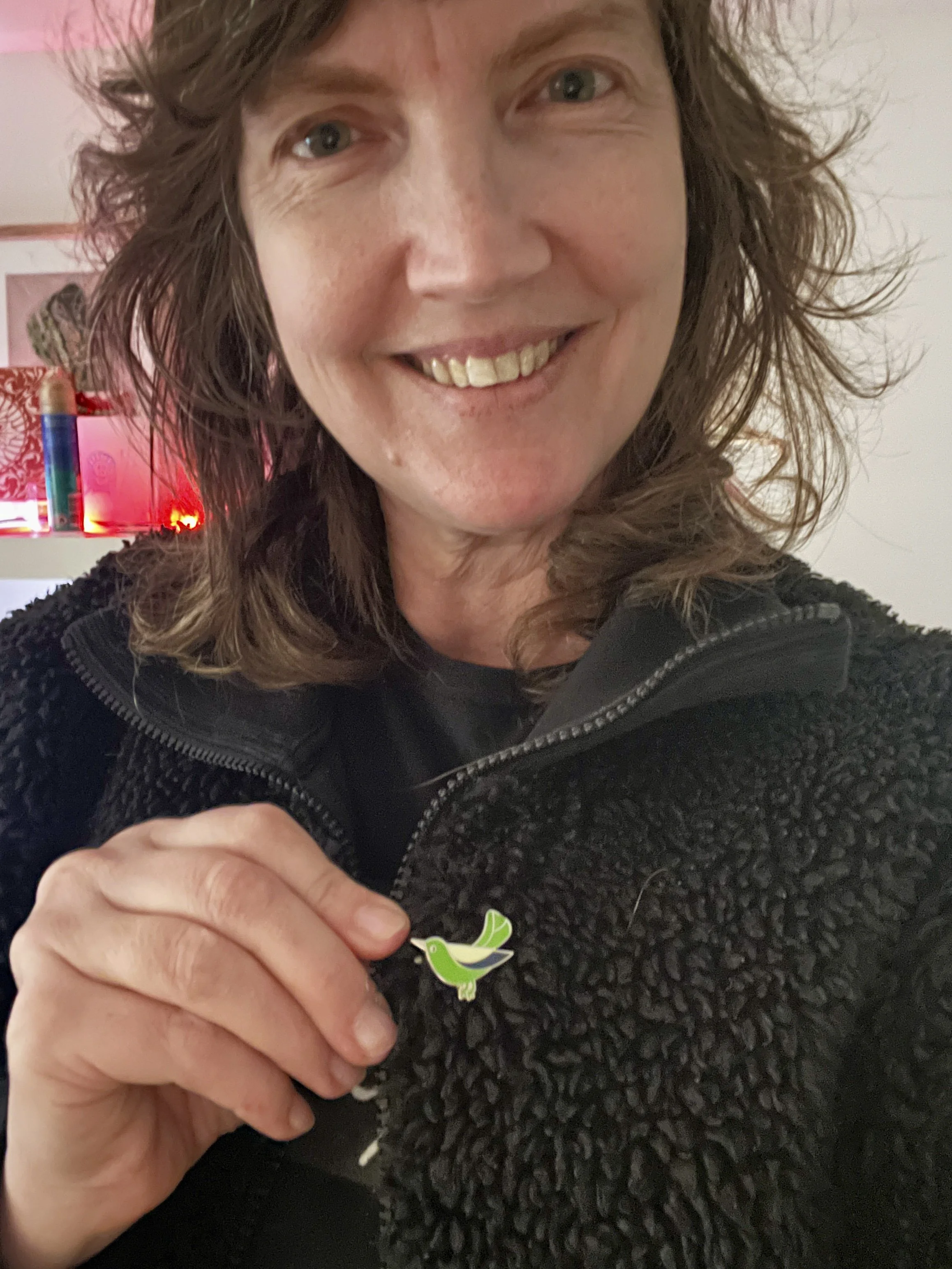 Green enamel lapel pin of a small bird mid-tweet