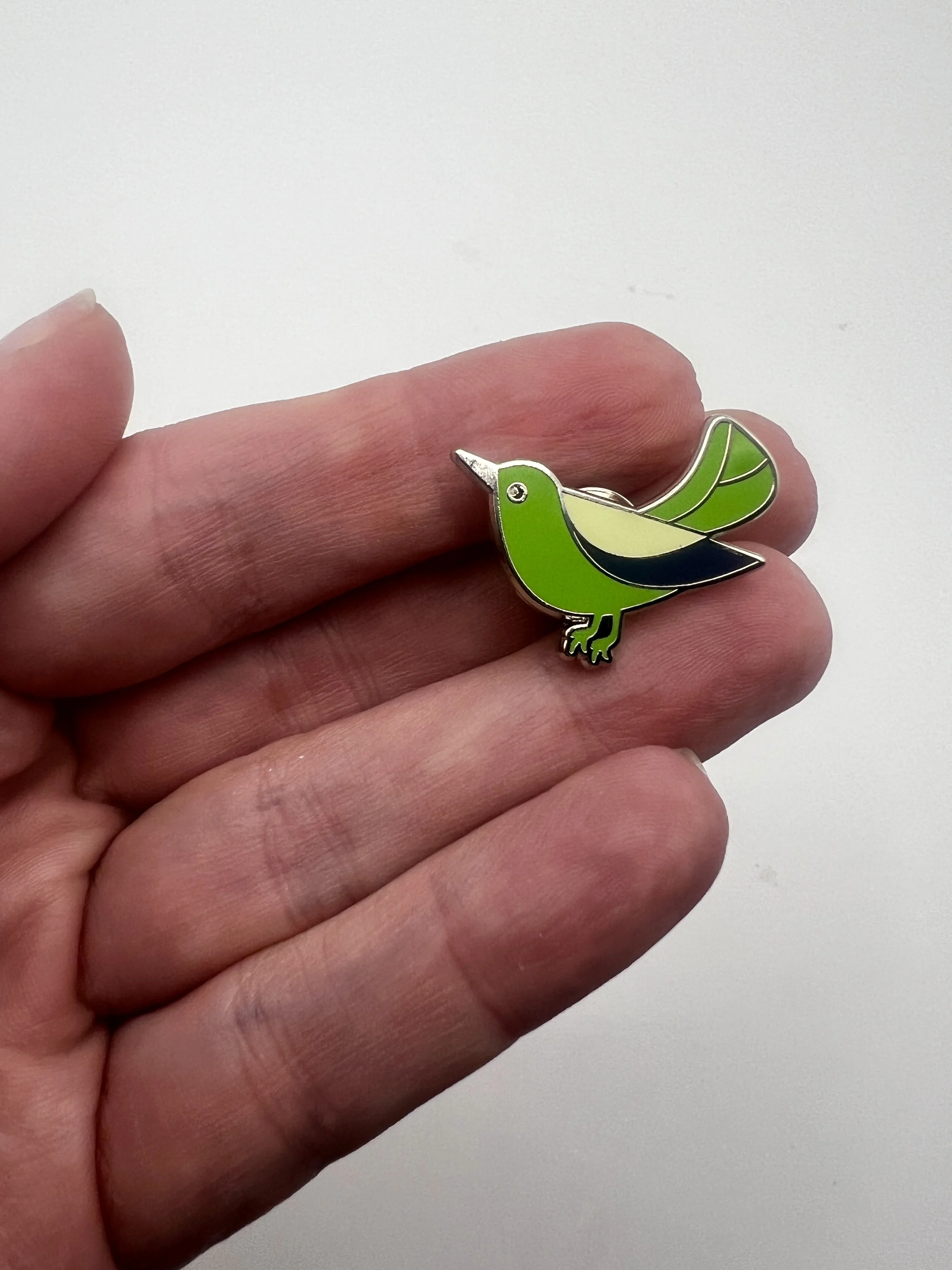 Green enamel lapel pin of a small bird mid-tweet