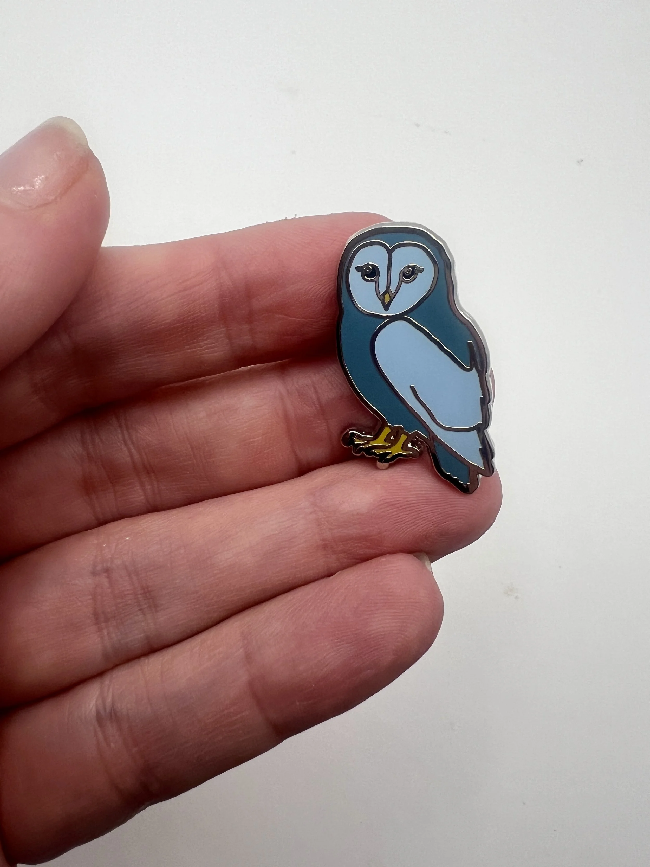 Blue enamel lapel pin of a small owl mid-hoot