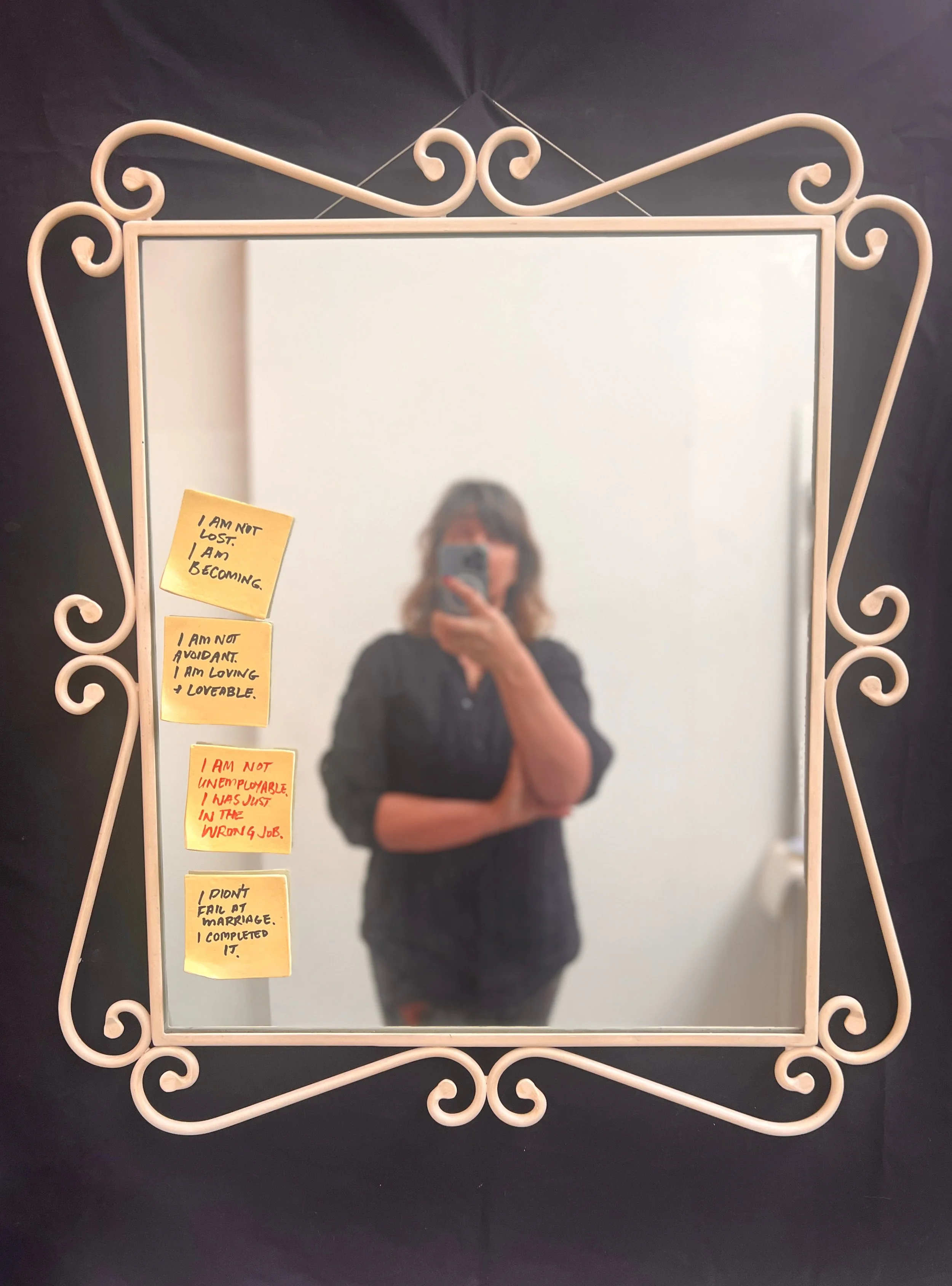 Photograph of framed mirror with ceramic recreations of post-it notes adhered and the artist taking the photo as a slightly blurred reflection.