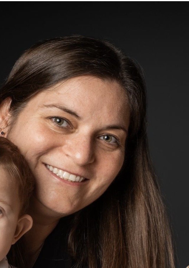 Close-up of a woman with long brown hair smiling against a dark background.