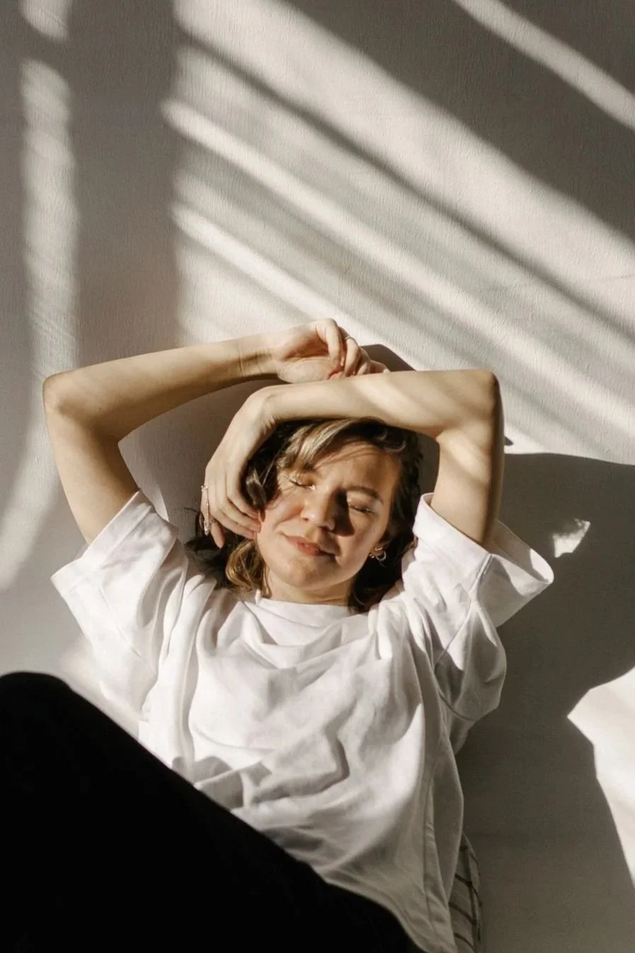 Woman relaxing in bed with eyes closed, representing rest, sleep, and nervous system recovery