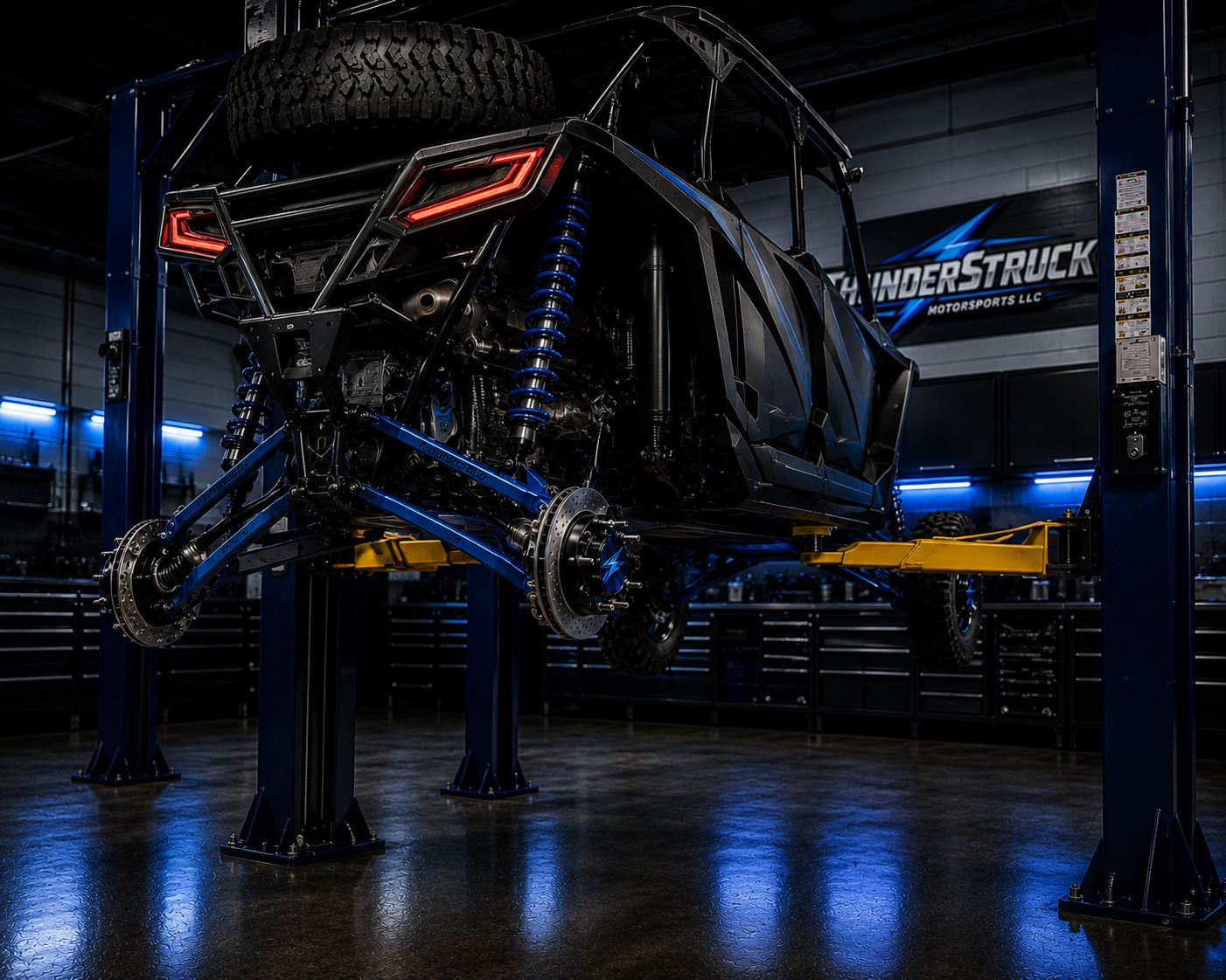 Off-road racing vehicle on lift in garage with Blue and black color scheme and neon lighting.