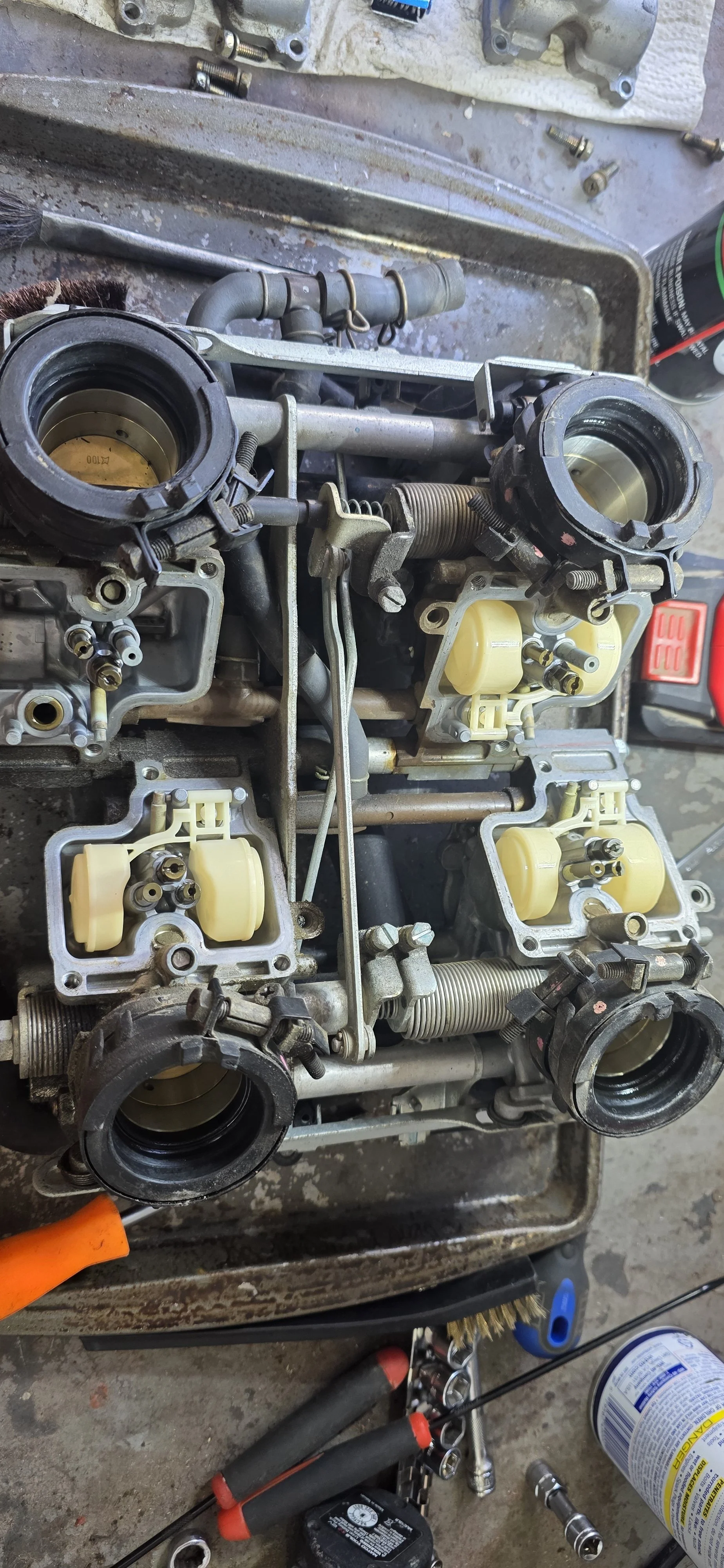 A disassembled carburetor with various parts and tools surrounding it, placed on a workbench.