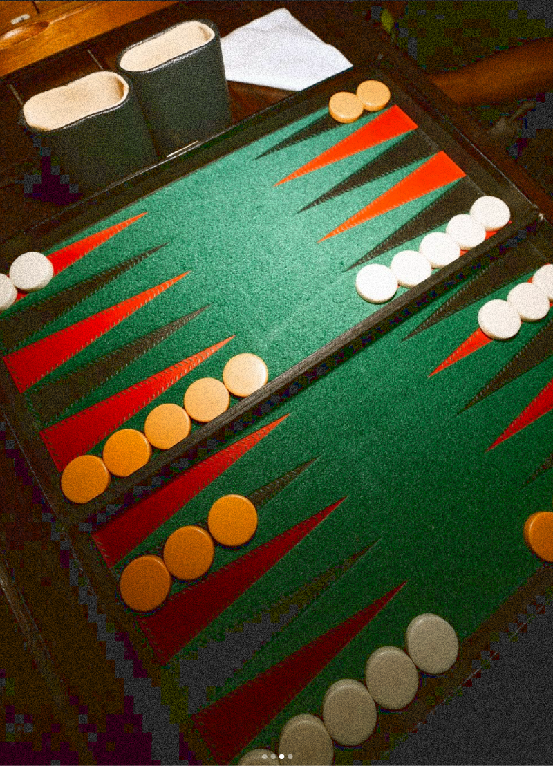 A backgammon board with orange and white checkers, two white cups, and a white cloth on a wooden table.