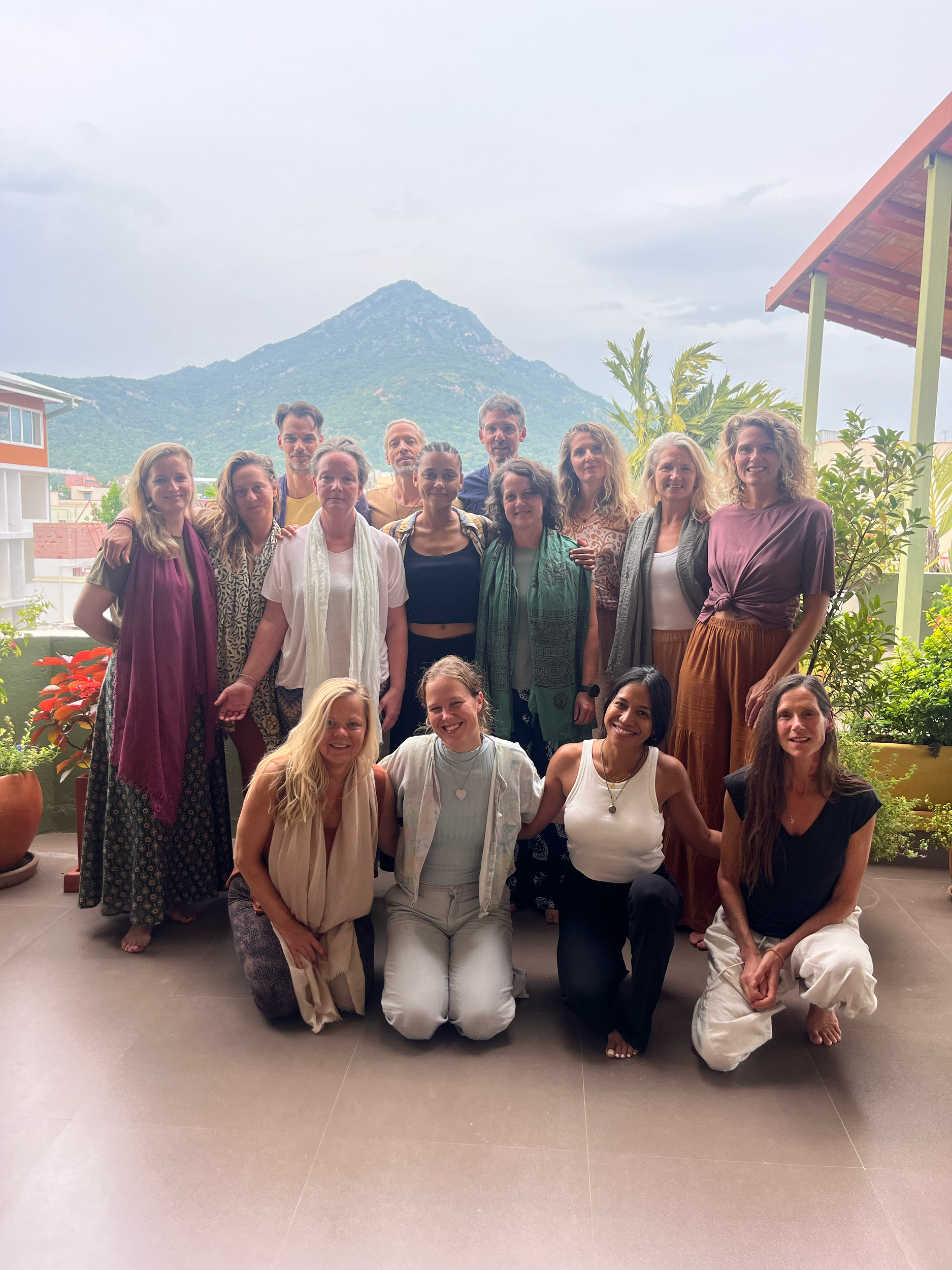 A group of people posing together on a balcony with mountains and greenery in the background.