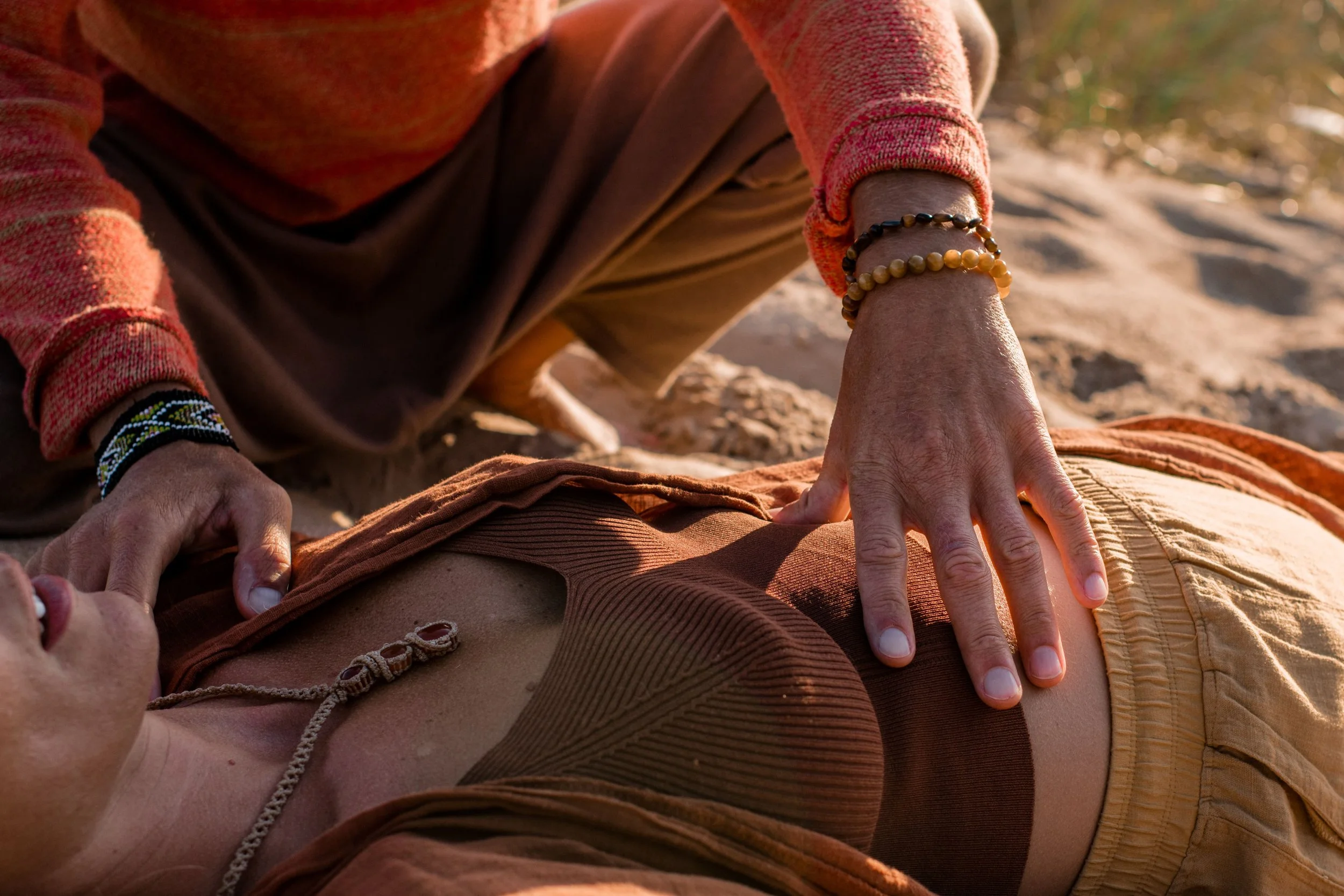 Person receiving a massage outdoors, wearing a red-orange sweater and jewelry, with hands on their back.