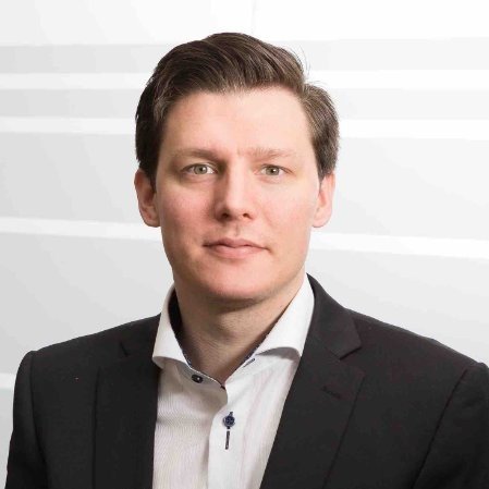 Portrett av en mann i formell sorte dresser og hvit skjorte mot en lys bakgrunn.