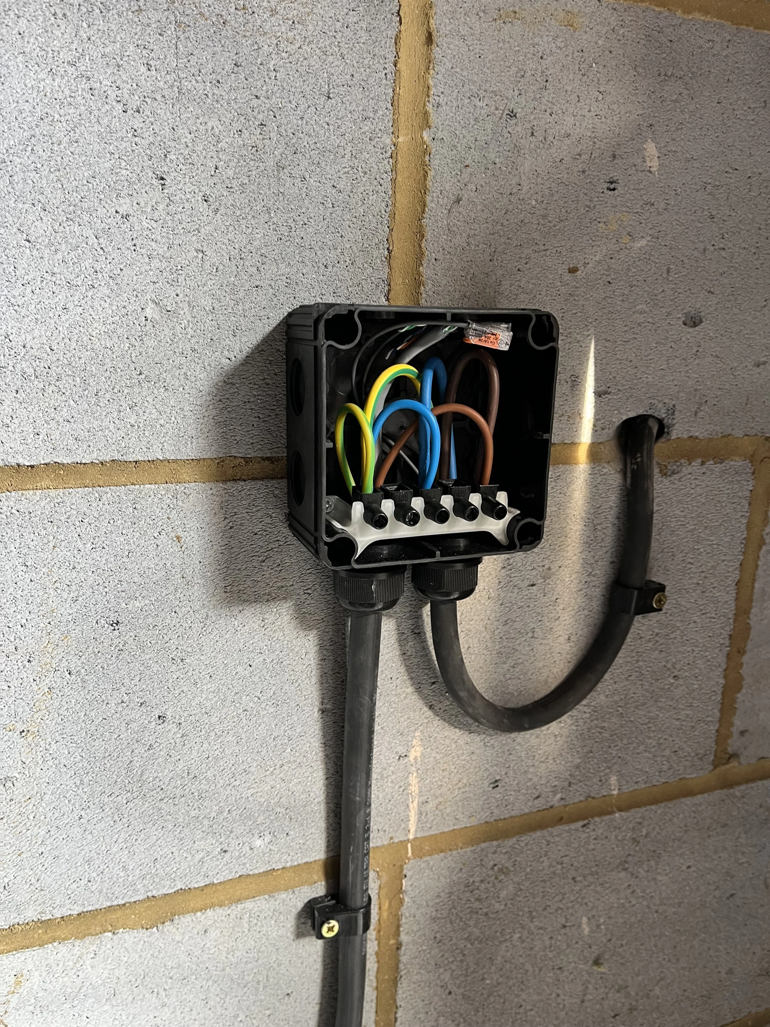 Electrical box with exposed wires and conduit pipes mounted on a wall, partially open with wires visible inside.