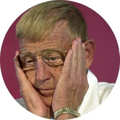 Close-up of an elderly woman wearing glasses, holding her face with her hands, showing a worried or distressed expression.