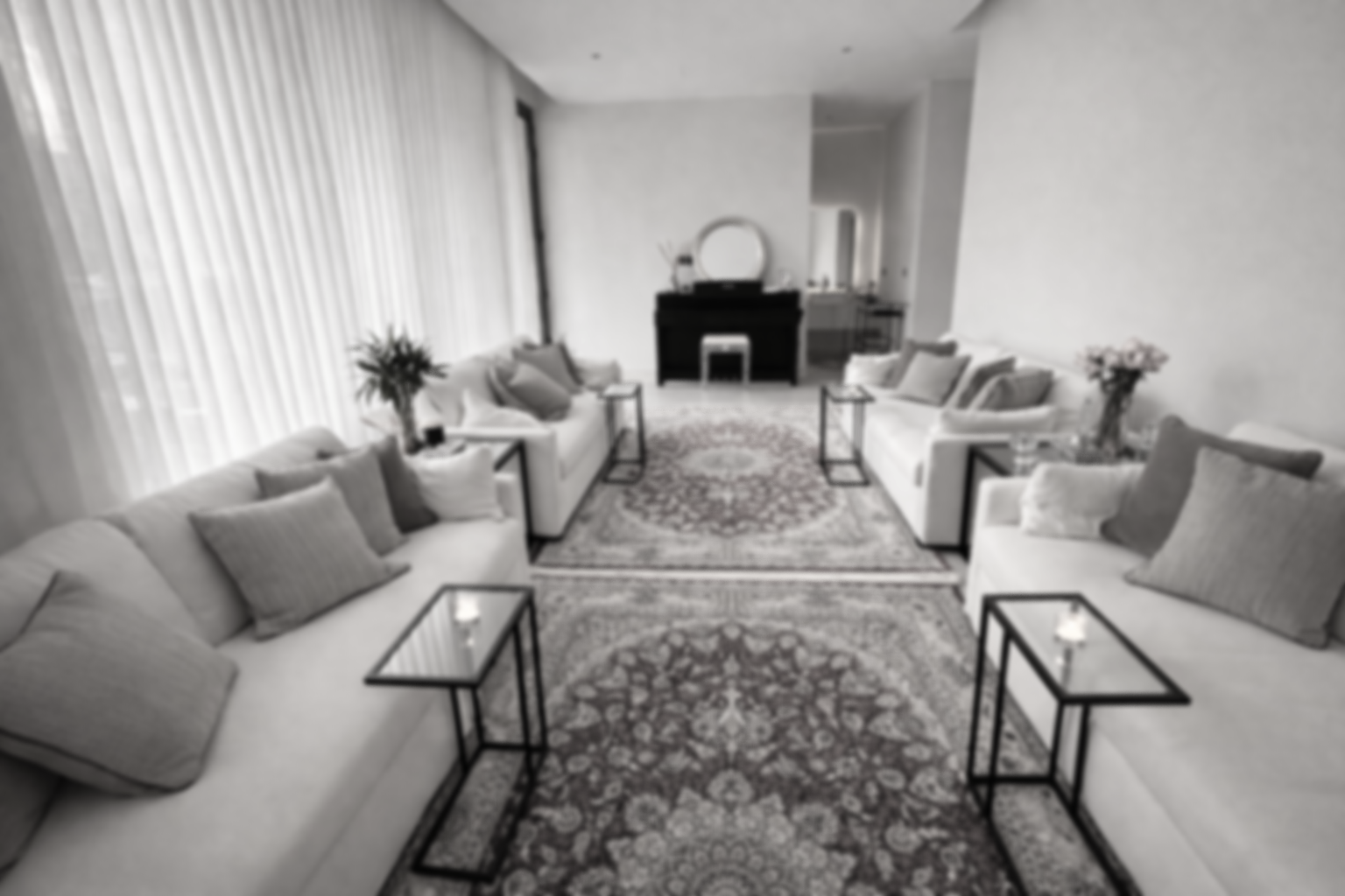 Une salle de séjour élégante avec canapé et fauteuils blanc, tapis orné, tables avec bougies, et un piano noir en fond.