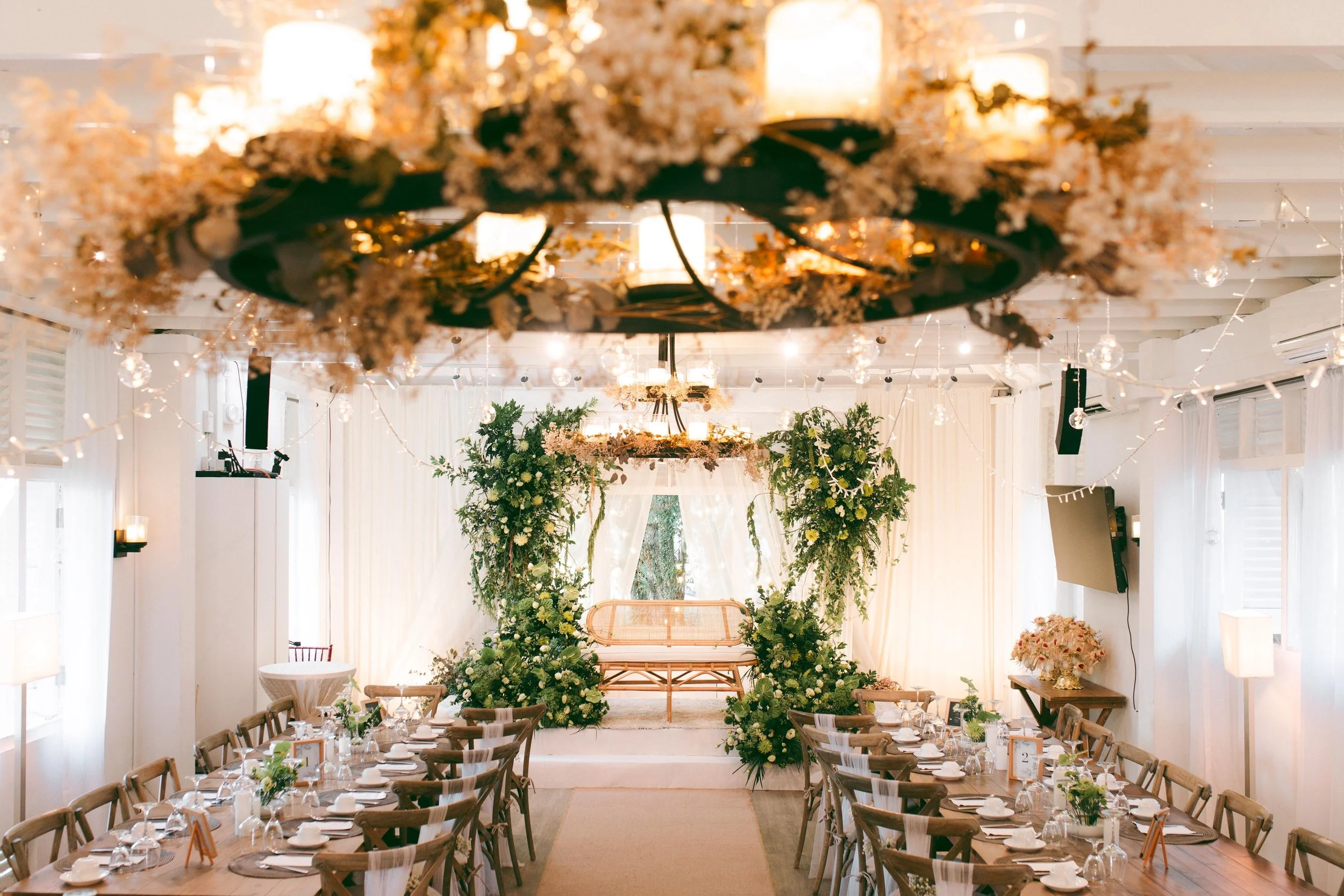 Elegant indoor wedding reception with decorated tables, floral arrangements, and a floral arch at the altar.