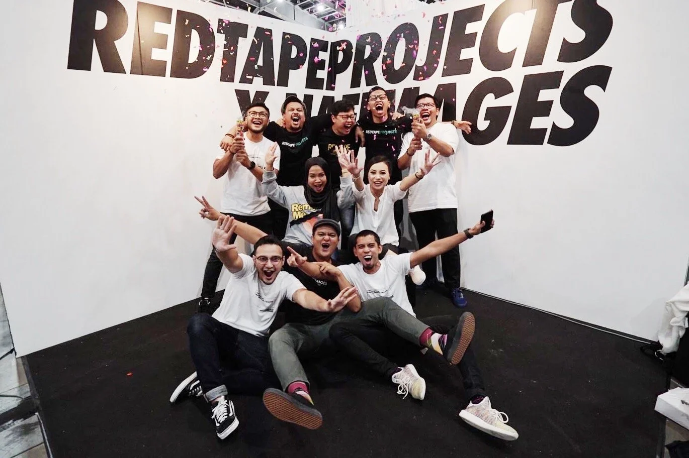 Group of happy people celebrating in front of a white wall with large black letters that say 'REDTAPROJECTS & NAFIMAGES' at an event or conference.