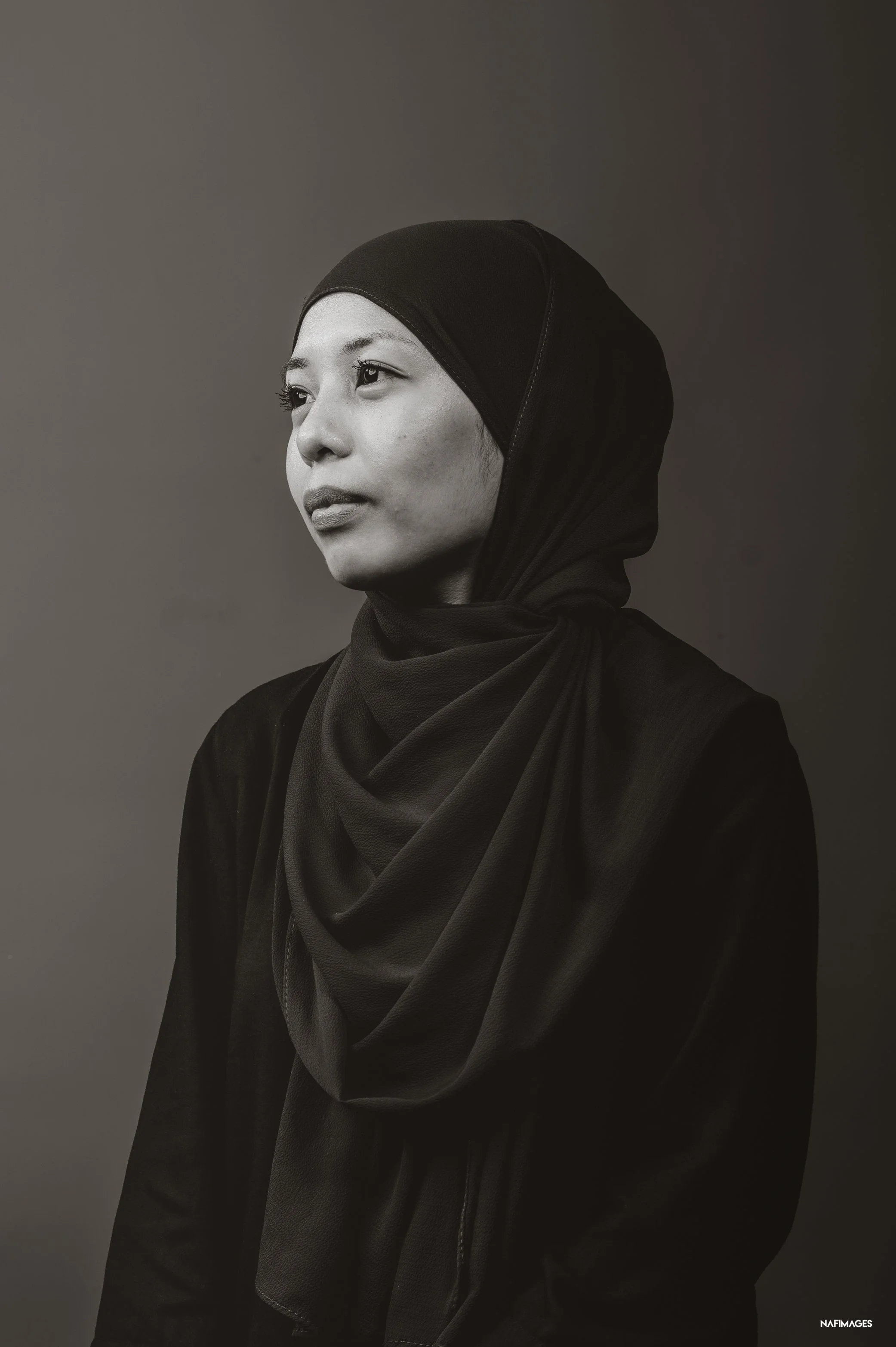 Portrait of a woman wearing a hijab, looking to her left, in a black and white photograph.
