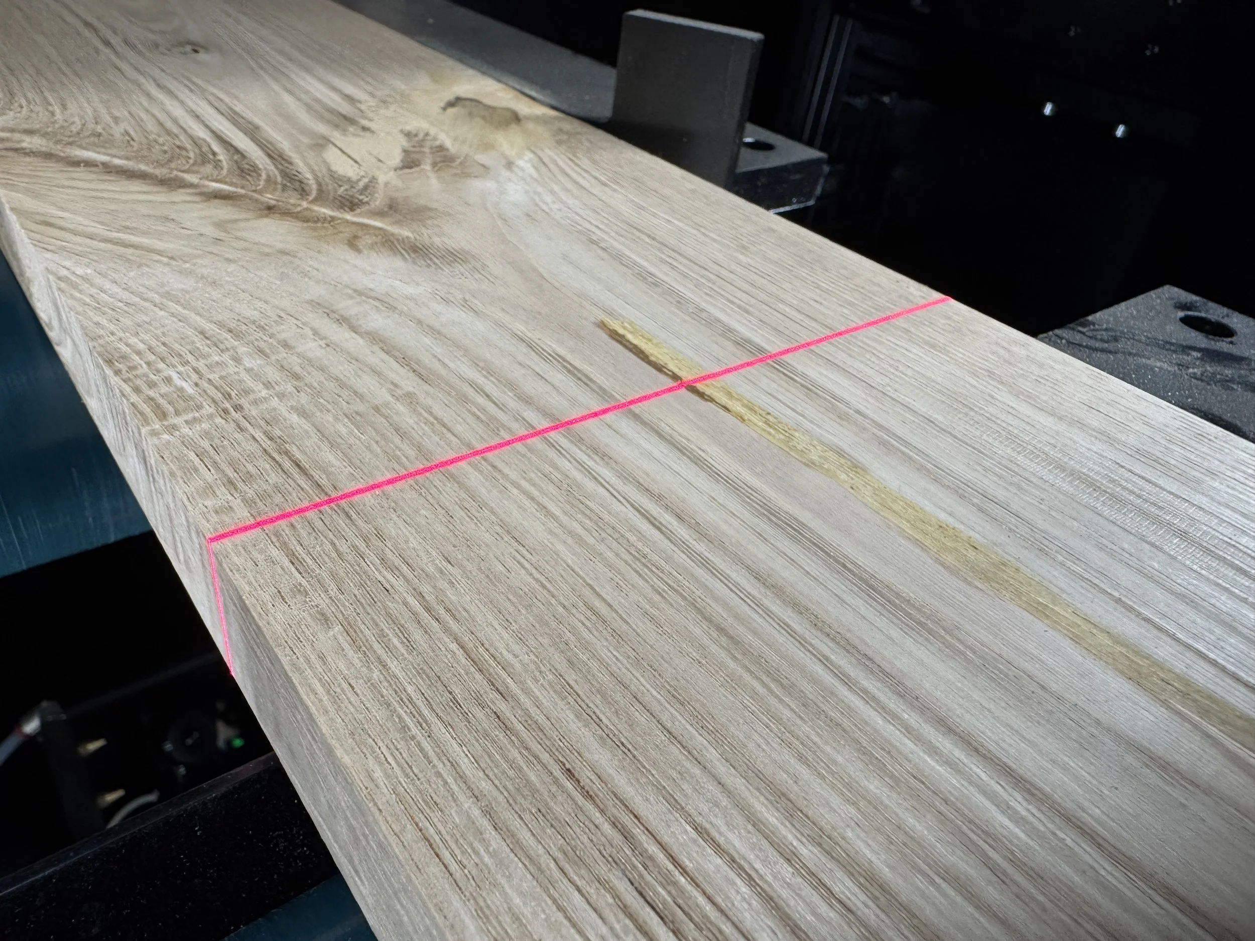 Una tavola di legno con una linea laser rossa proiettata che attraversa il suo spessore per ispezione del legno con scansione laser 3D.