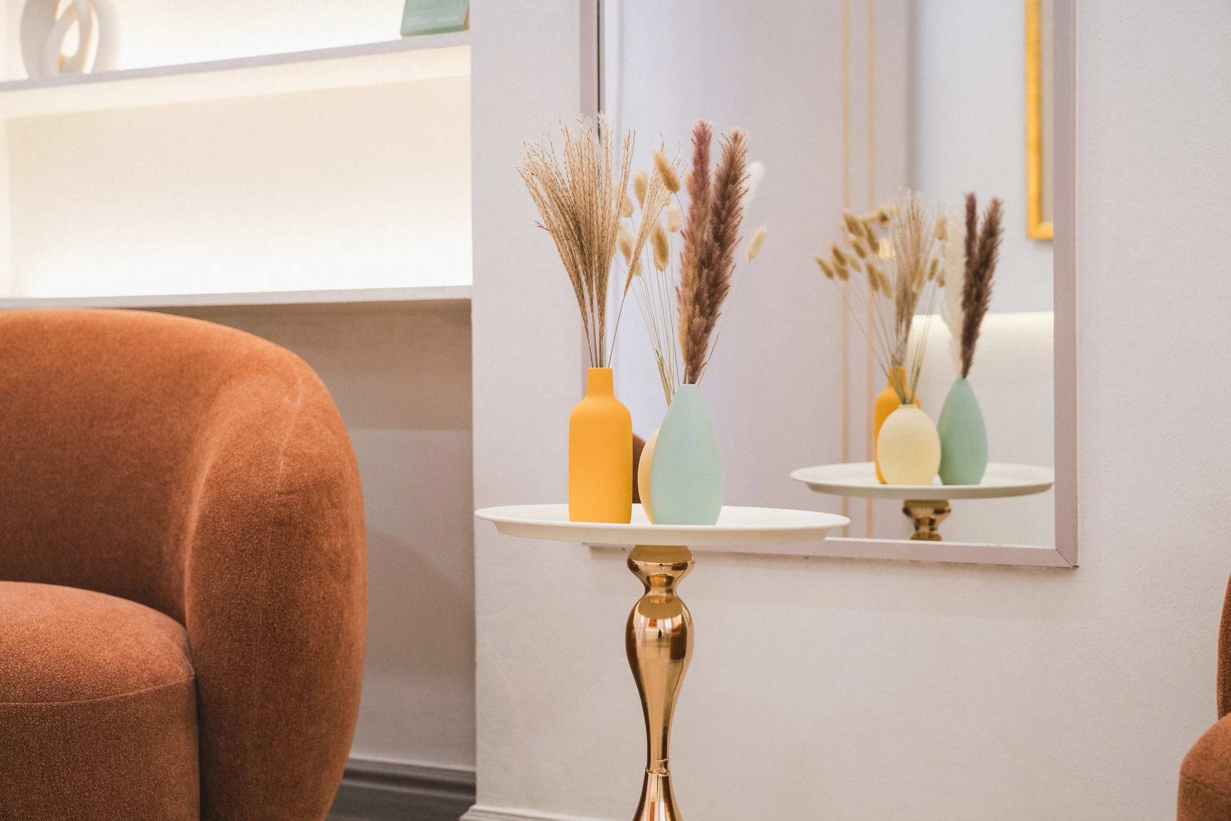 Decorative vases with dried plants on a small table in front of a mirror in a living room.
