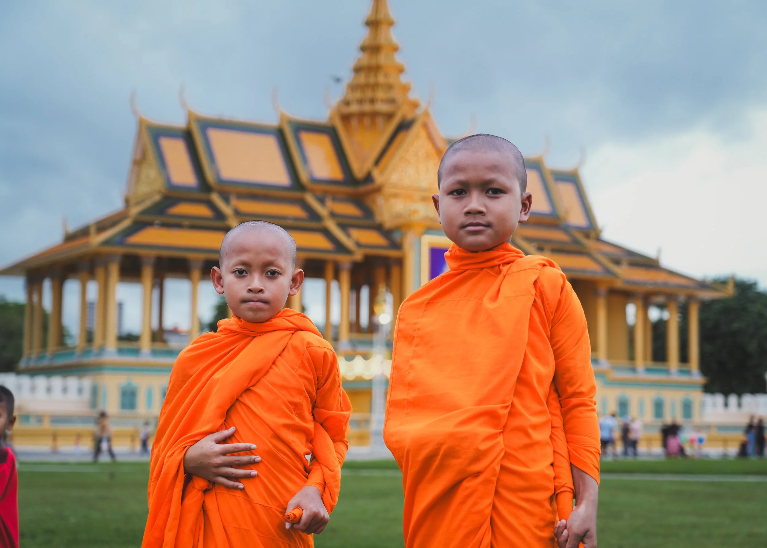 Two young Buddhist monks in orange robes standing in front of a historical temple with intricate architecture during daytime.