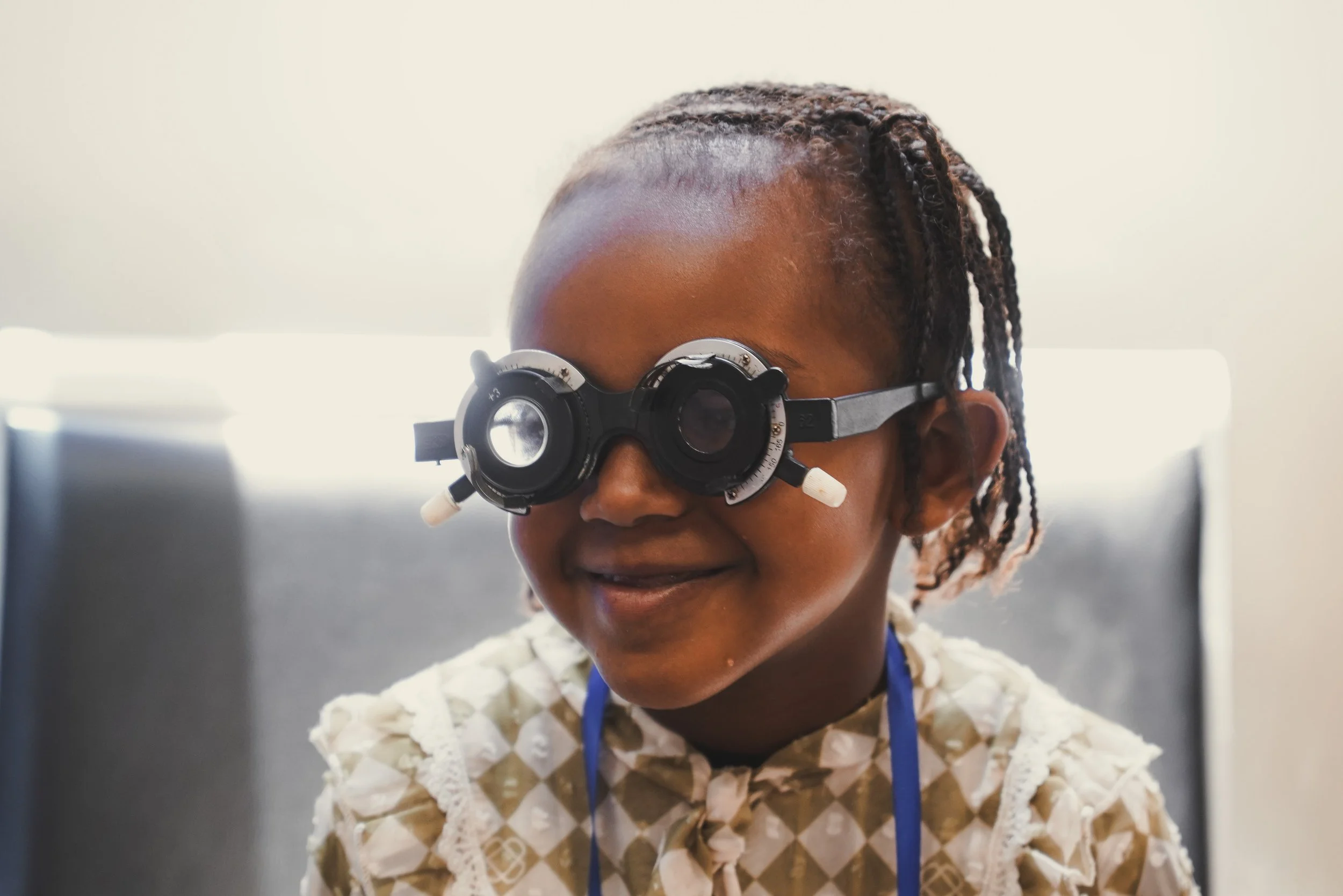 Young girl with braided hair wearing magnifying glasses, smiling.