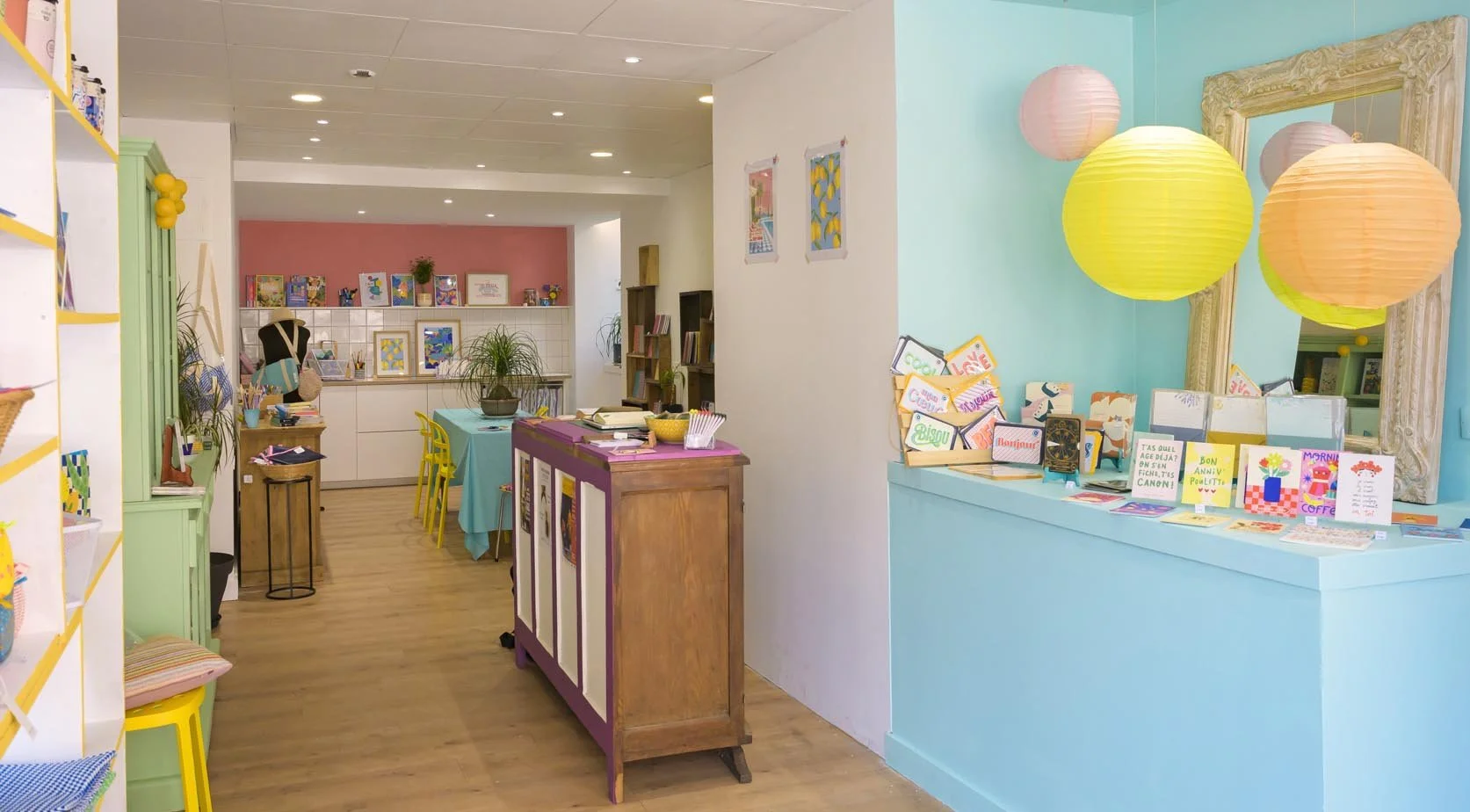 Intérieur d'une boutique ou d'un atelier créatif avec luminaires colorés, livres, affiches, et étagères pleines d'articles colorés.