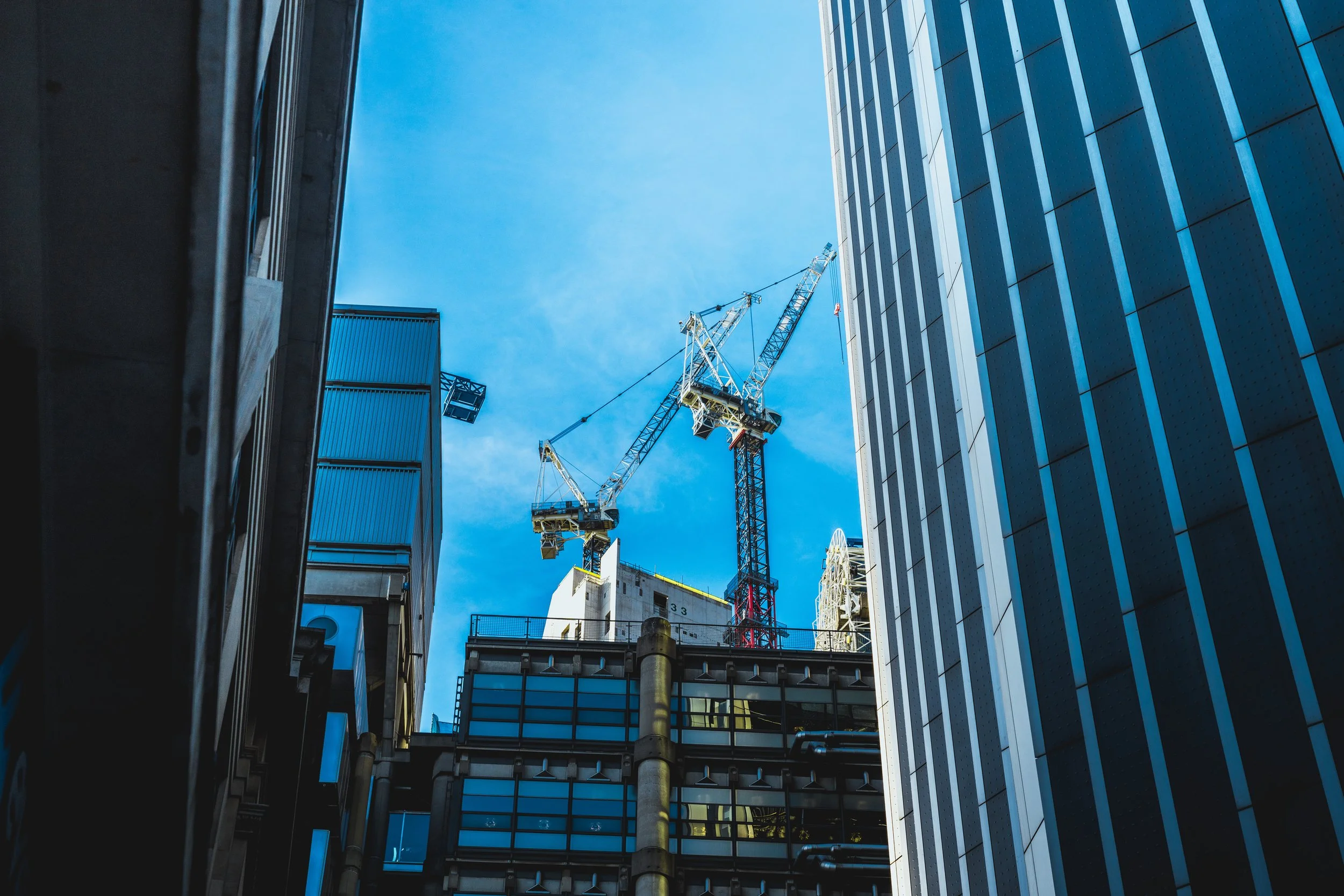 Looking up between two modern skyscrapers with reflective glass facades; a construction crane stands in the background against a clear blue sky.