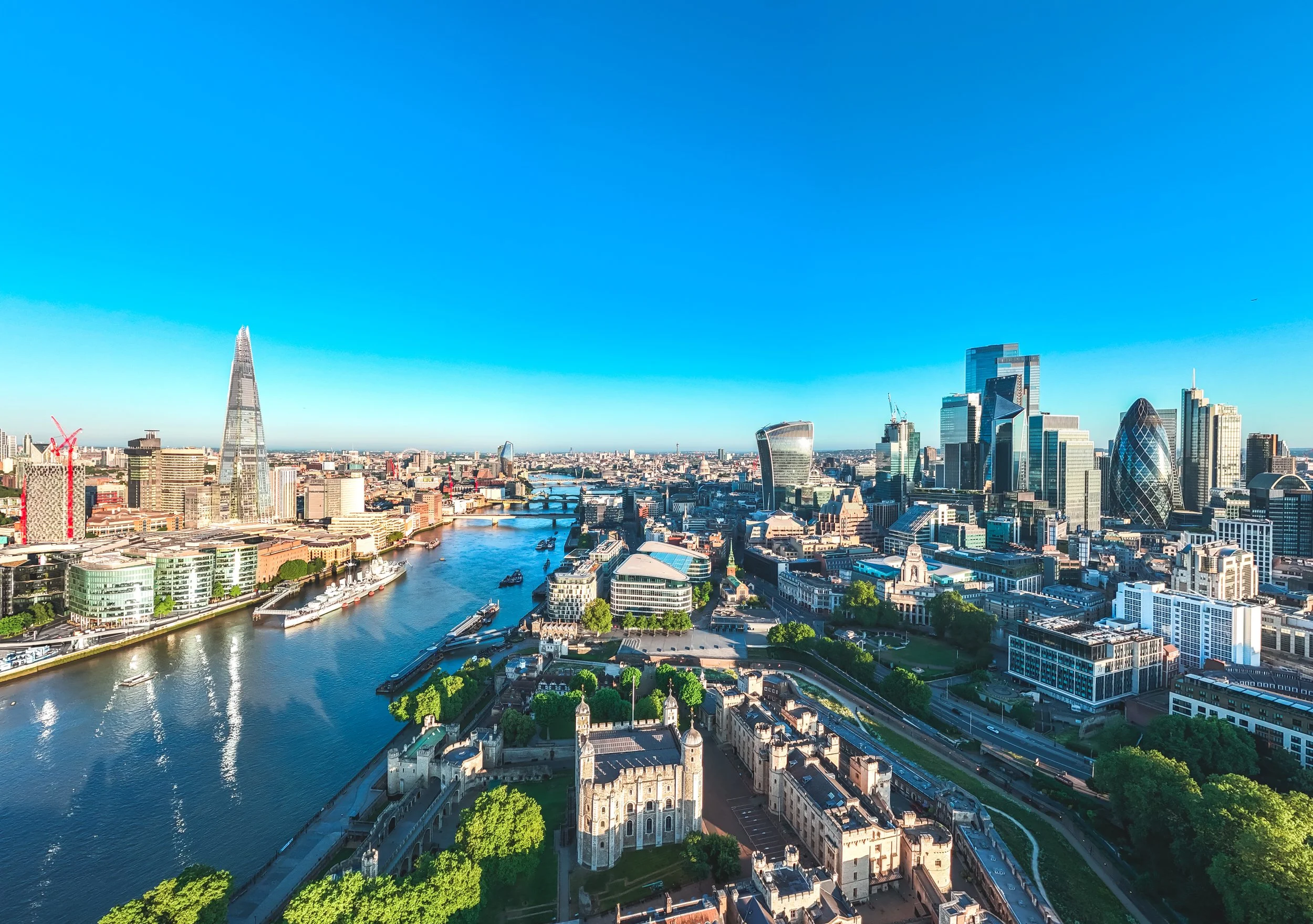 A panoramic view of London's skyline featuring modern skyscrapers, the River Thames, and historical landmarks under a clear blue sky.