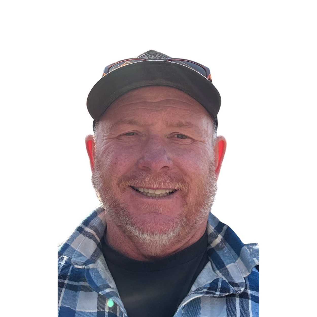 Close-up of a smiling man wearing a black cap and sunglasses on top, dressed in a blue and white plaid shirt.