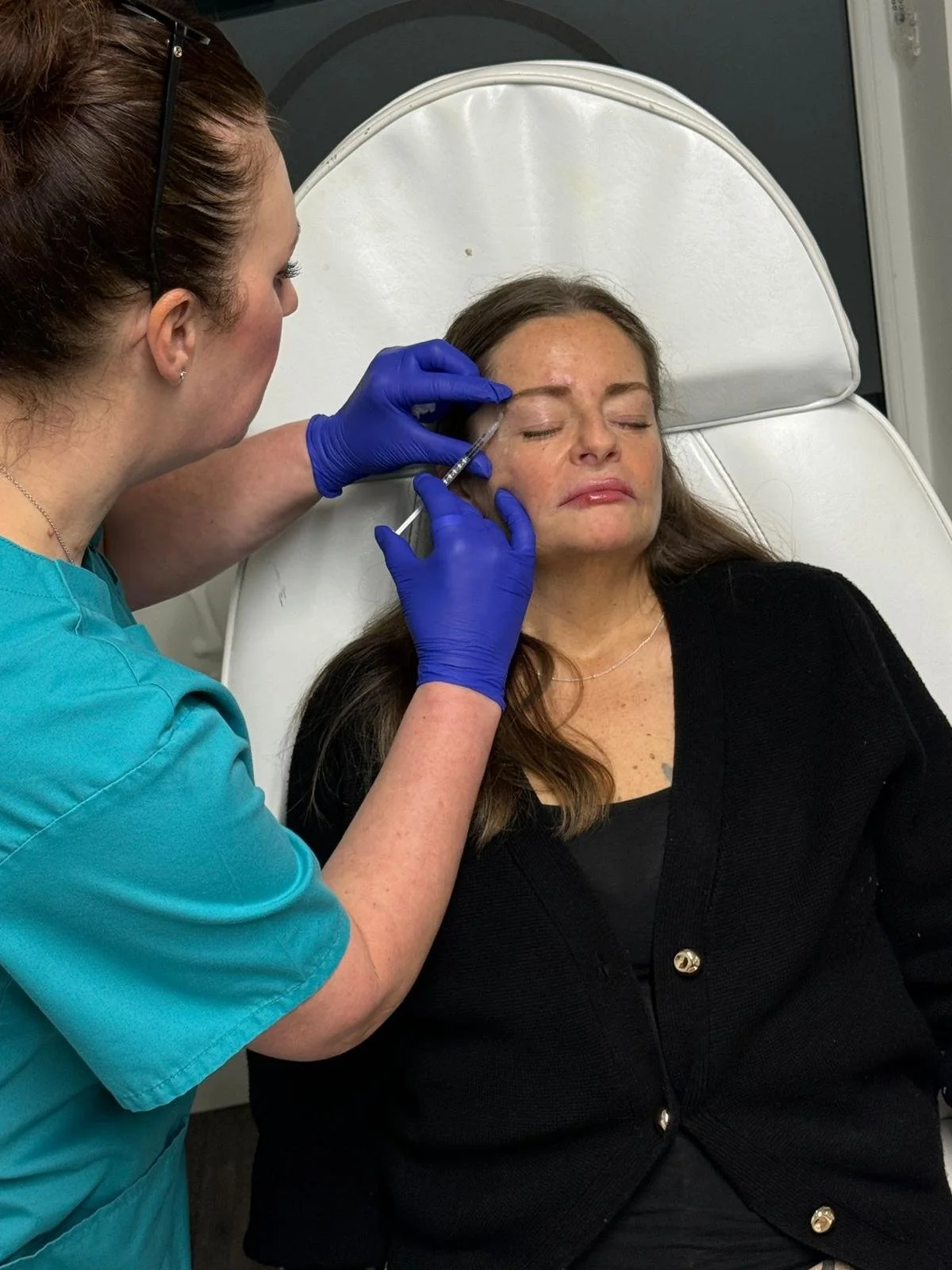 Medical professional administering Botox injections to a woman's forehead while she lies patiently on a treatment bed.