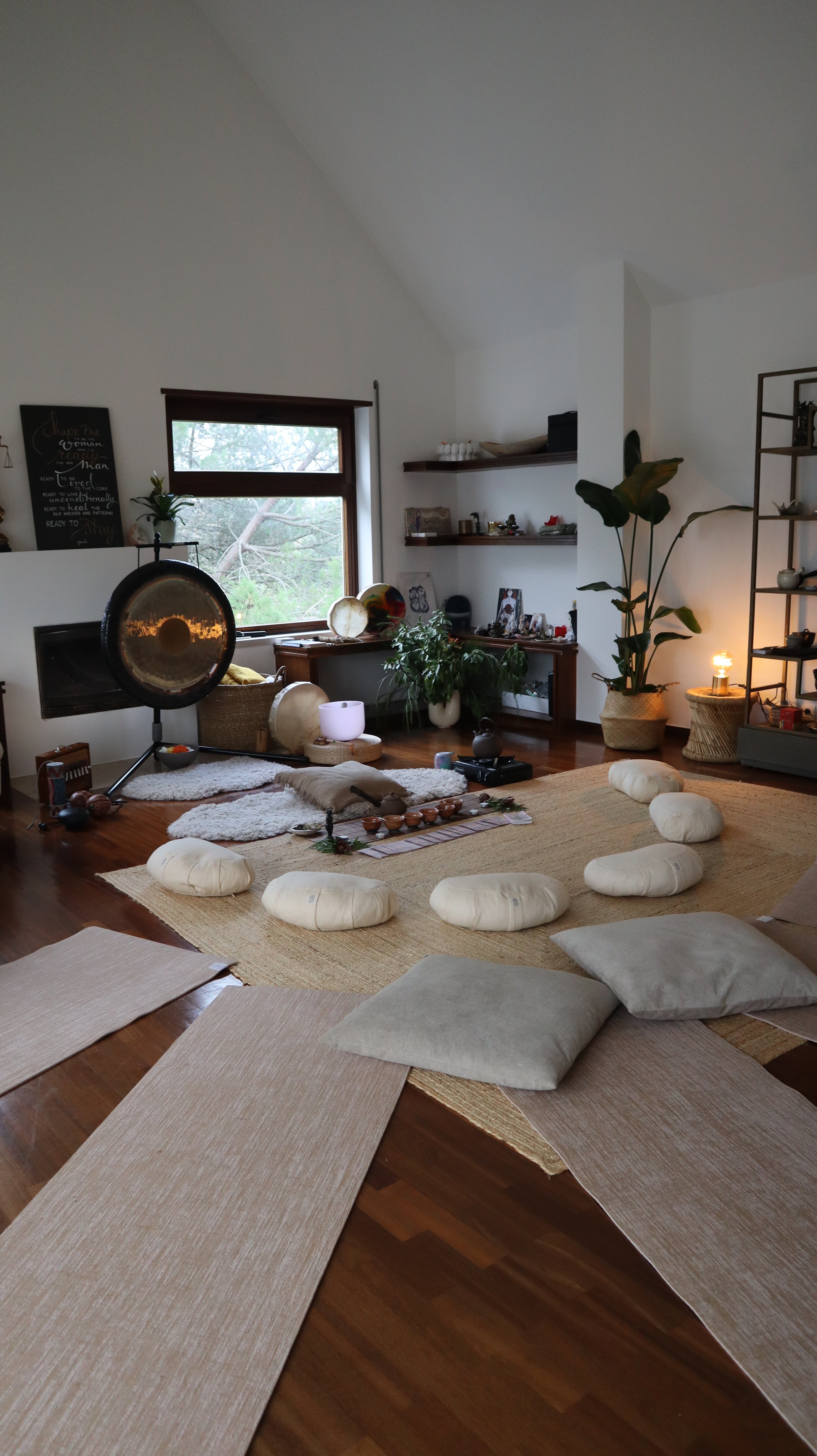 A cozy meditation and relaxation space with cushions, rugs, and calming decor, including a gong, plants, and soft lighting.