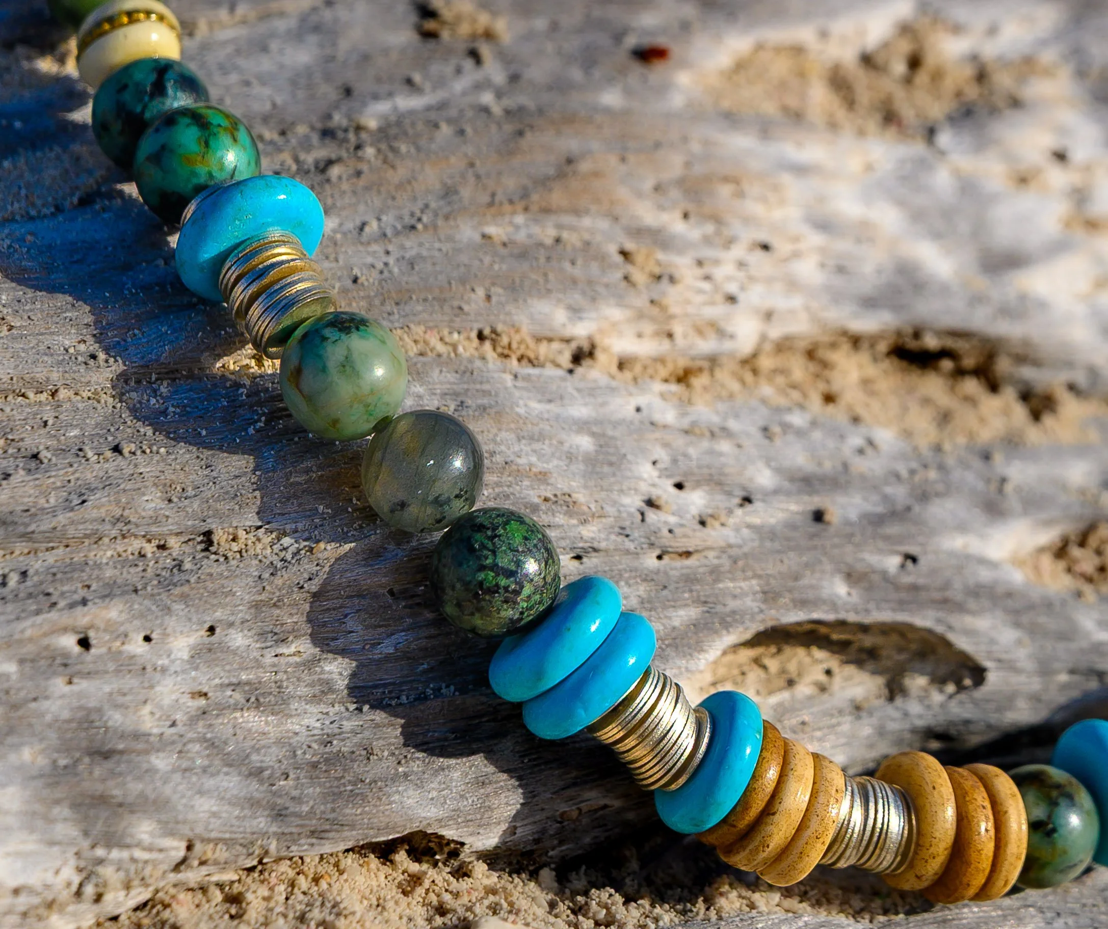 A string of colorful, round beads lying on a wooden surface, with some beads reflecting sunlight.
