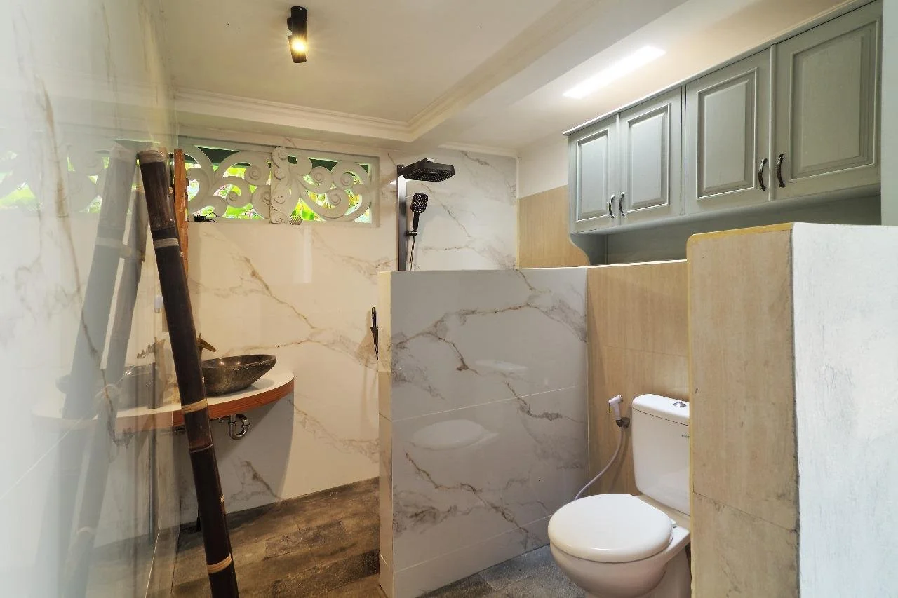 A modern bathroom with marble walls, a shower area with black showerheads, decorative vent with intricate carvings near the ceiling and storage space.