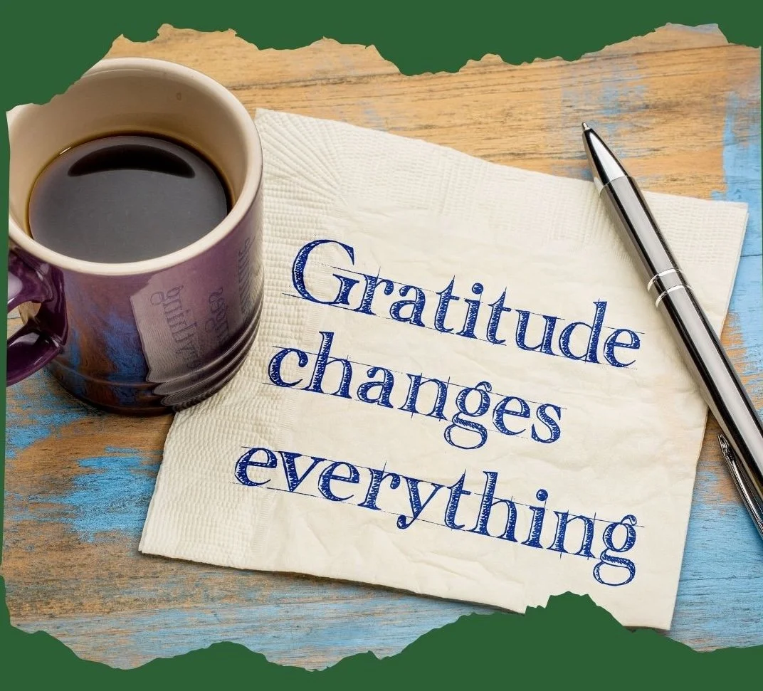 A cup of black coffee, a handwritten note with the phrase 'Gratitude changes everything', and a silver pen on a wooden surface.