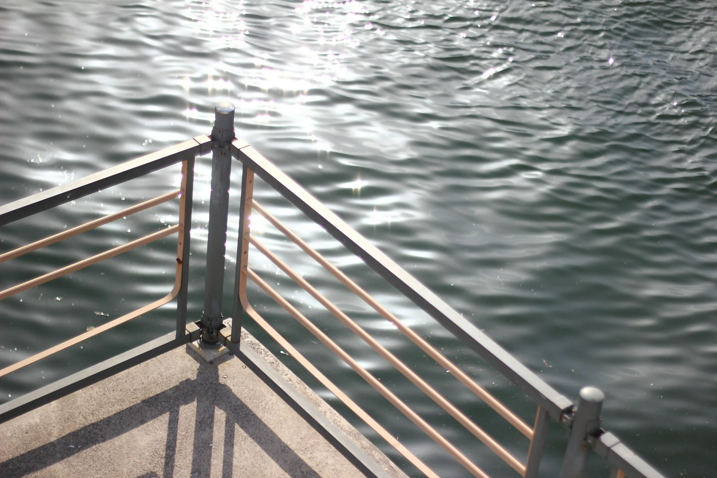 View of water with sunlight reflection, metal railing, and concrete platform.