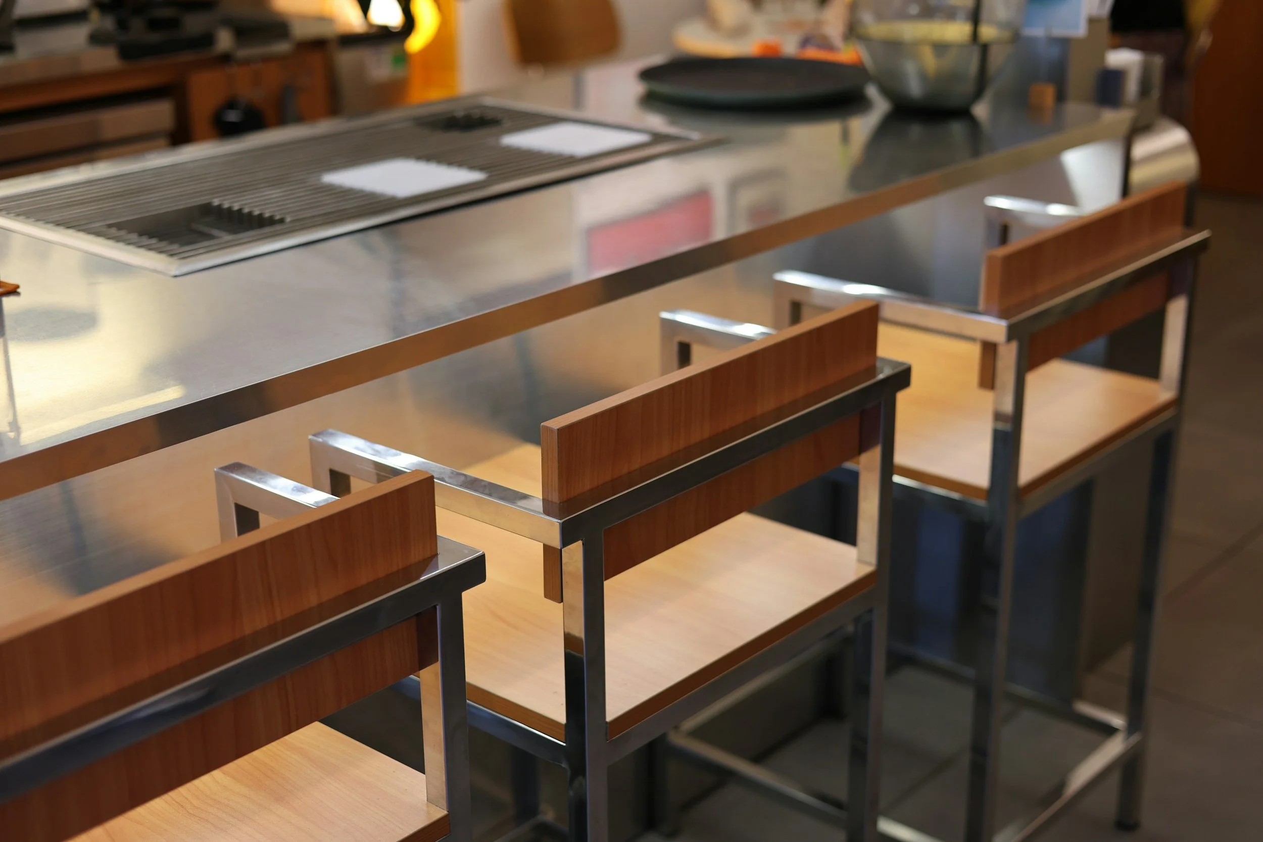 A row of bank-style stainless steel tables with wooden seats in a cafeteria or dining area.