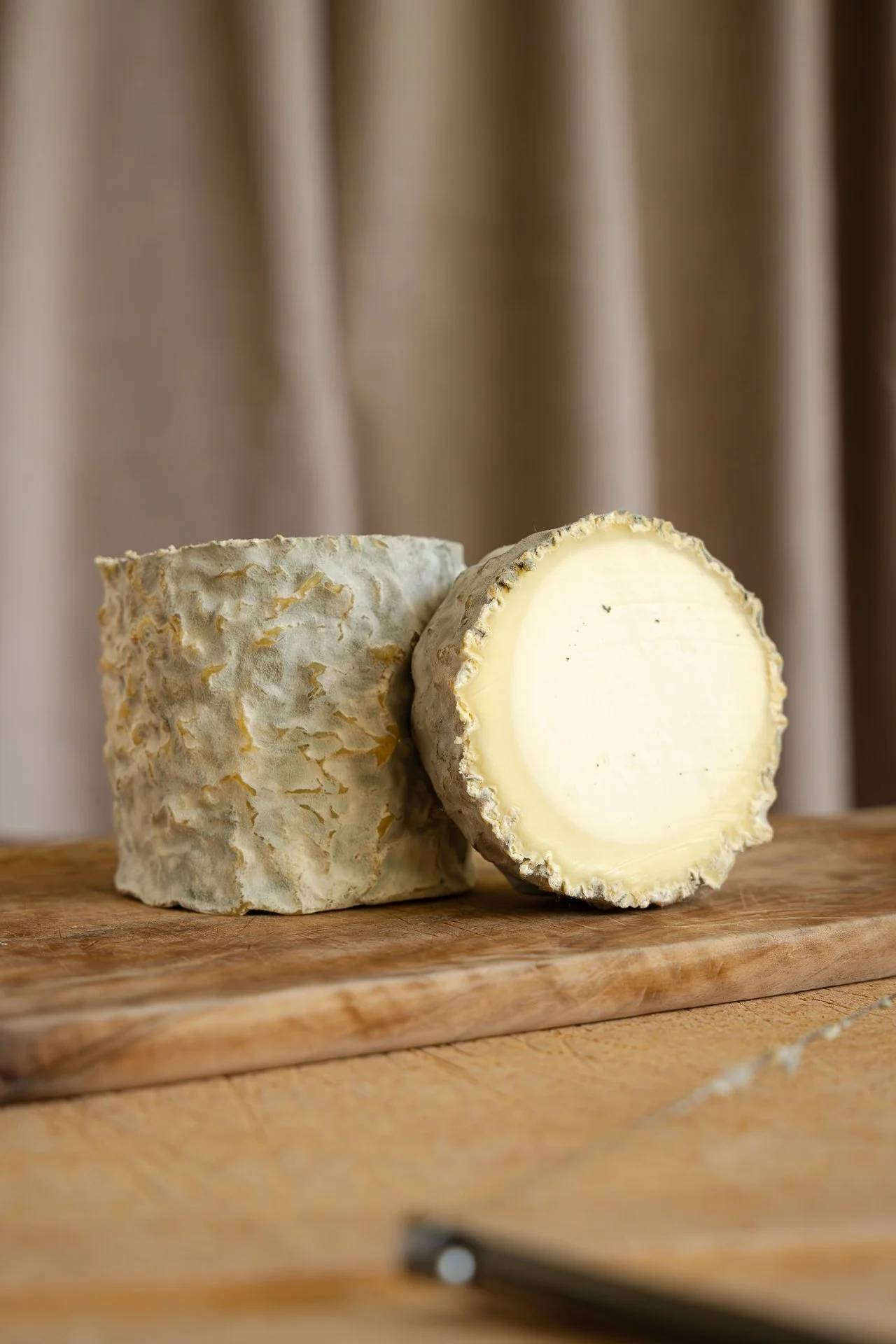 Clacbitou, un fromage de chèvre semblable à un Charolais, tranché pour révéler son cœur à la texture fine et soyeuse, et au contour crémeux. On aperçoit également sa croûte naturelle bleutée et ridée. Vue frontale.