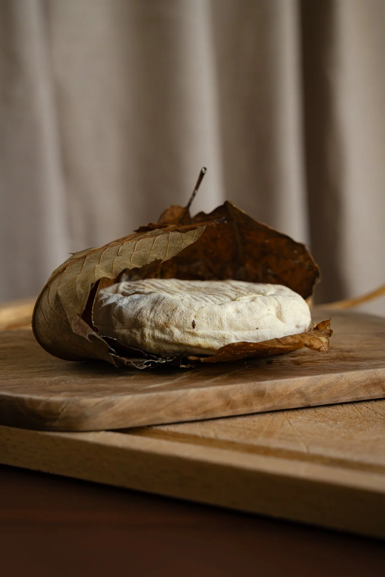 Fromage Banon AOP, déballé de ses feuilles de châtaignier et posé sur une planche en bois. Vue frontale.