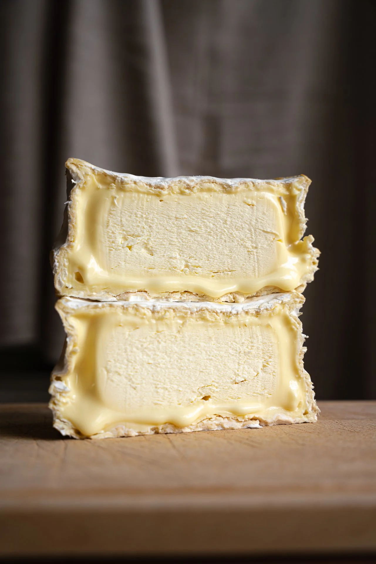 Fromage Chaource AOP coupé en deux. Les deux demis sont empilés l'un sur l'autre et posés sur une planche en bois. Sa texture est crémeuse, presque coulante.