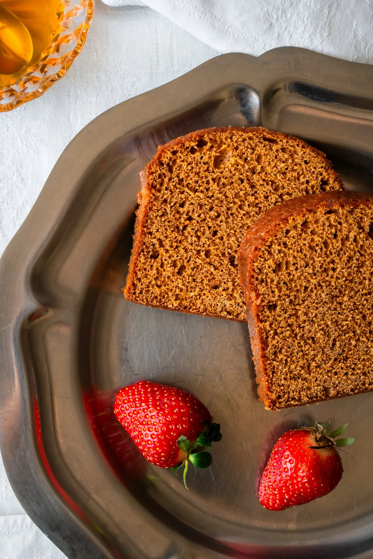 Tranches de pain d'épices, dans un plateau d'argent, accompagnés de fraises et de miel.