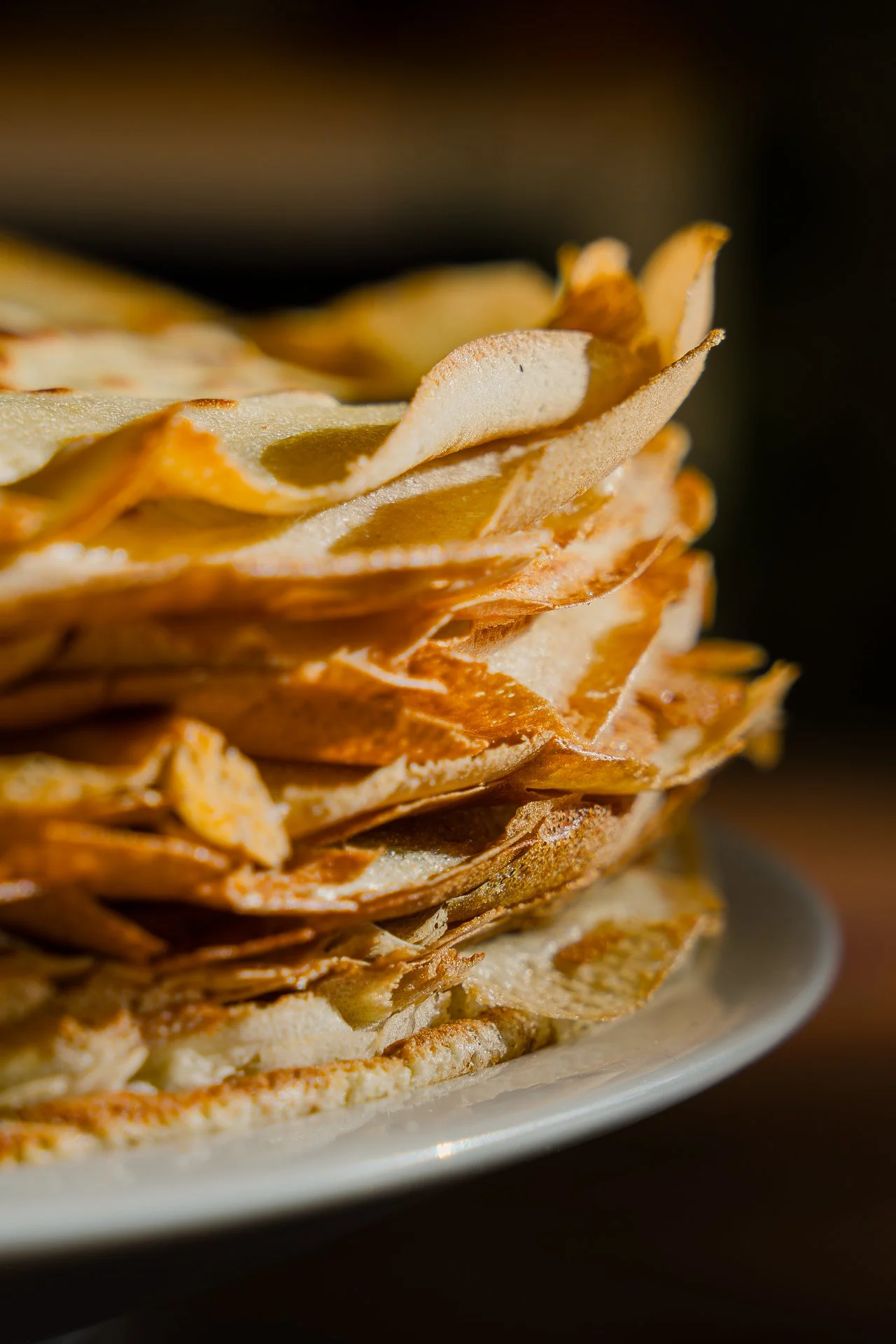 Une plie de crêpes en vue rapprochée, reposant dans une assiette blanche, sur un fond sombre et flouté.