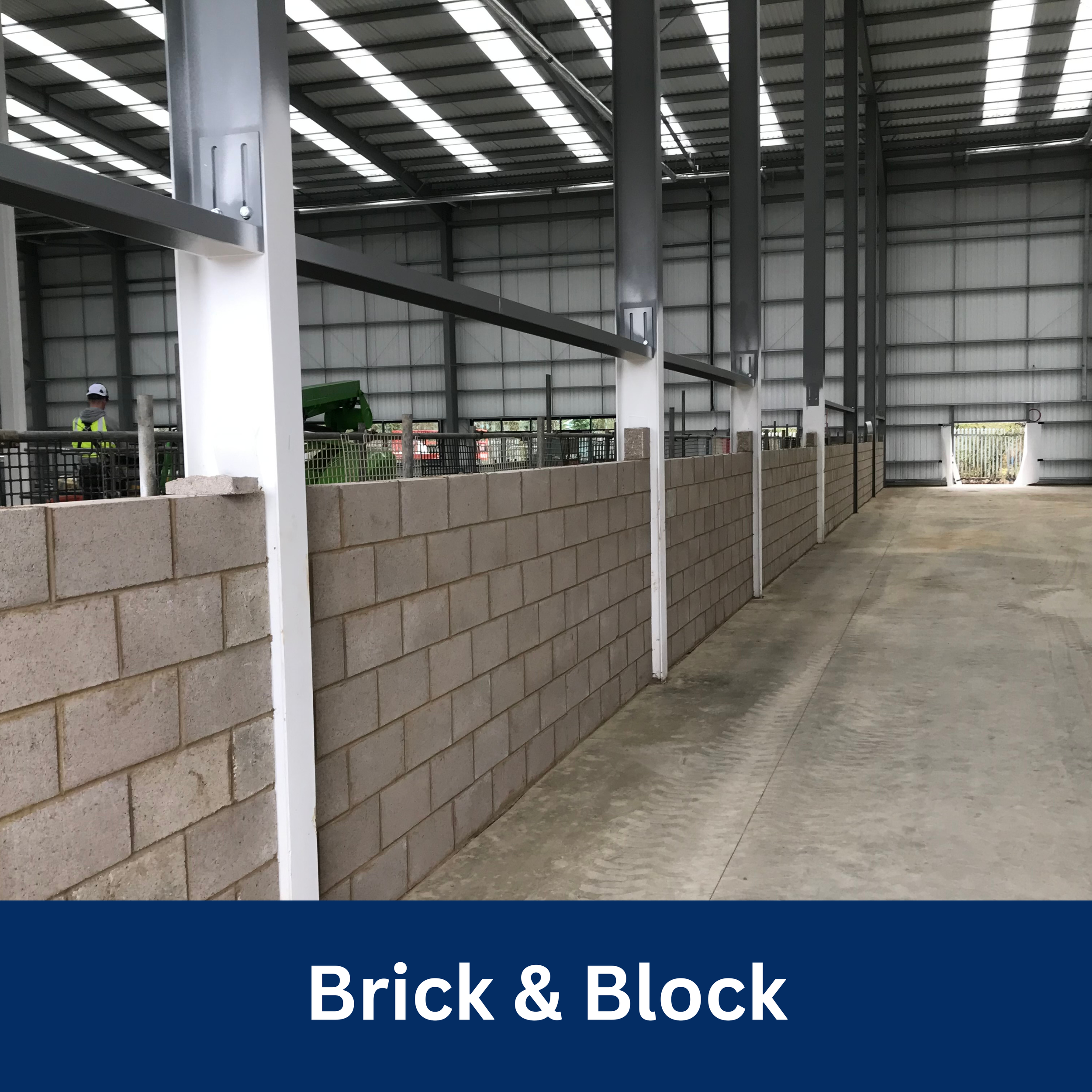 Interior of a warehouse with a brick wall and steel beams, with a person in a high-visibility vest near the back.