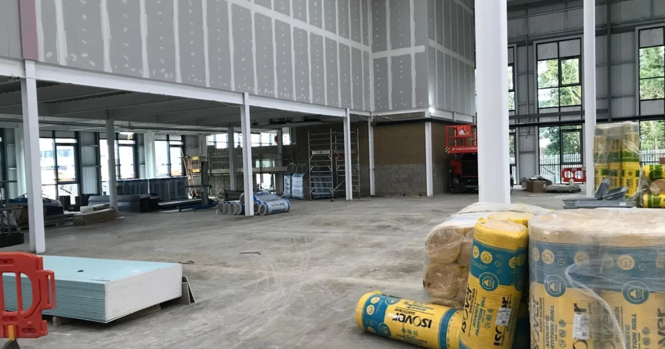 Interior of a building under construction with insulation, scaffolding, and construction materials scattered on the floor.