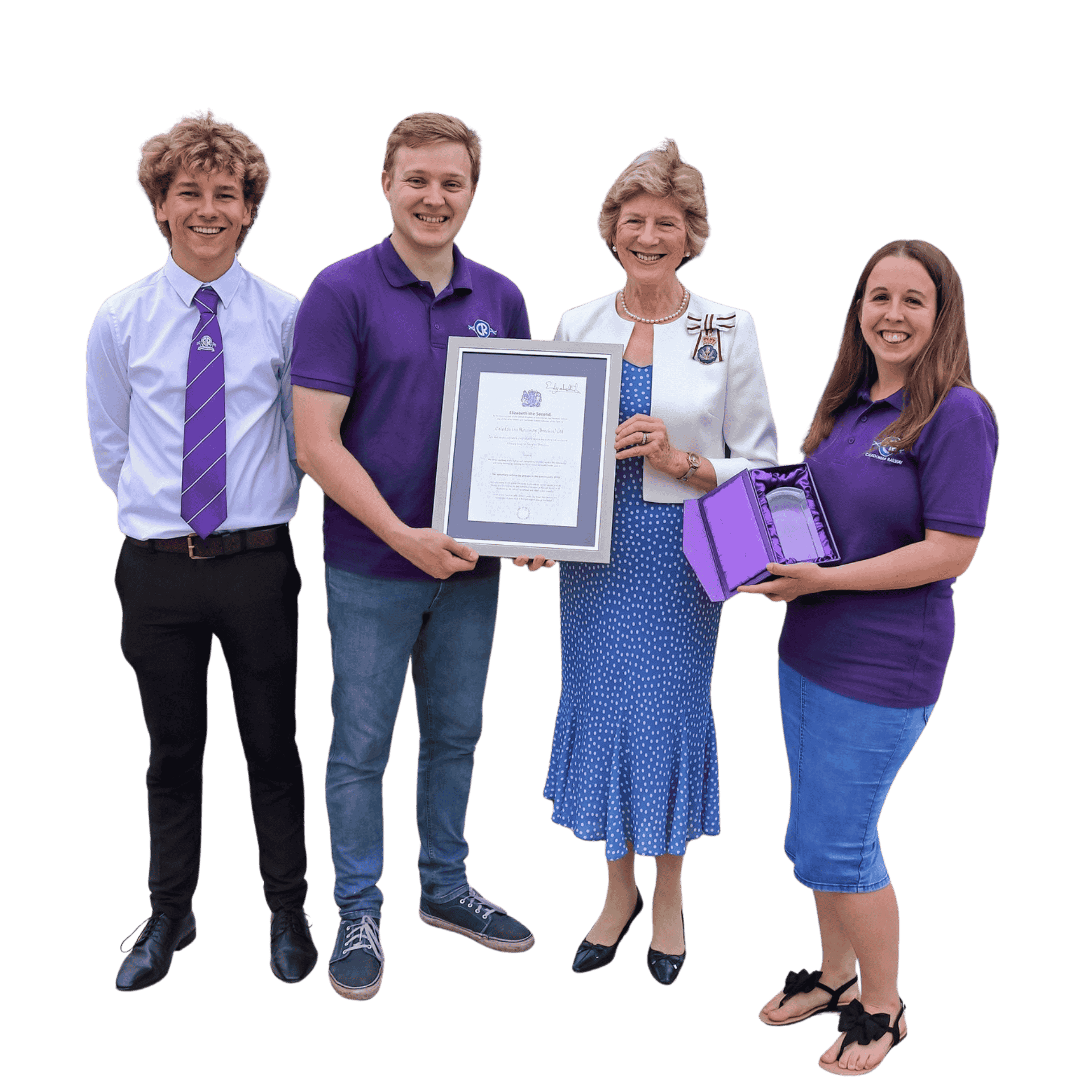 Four volunteers standing together, smiling. The woman in the middle is holding a framed certificate. The girl on the right is holding a purple box celebrating their volunteering achievement.