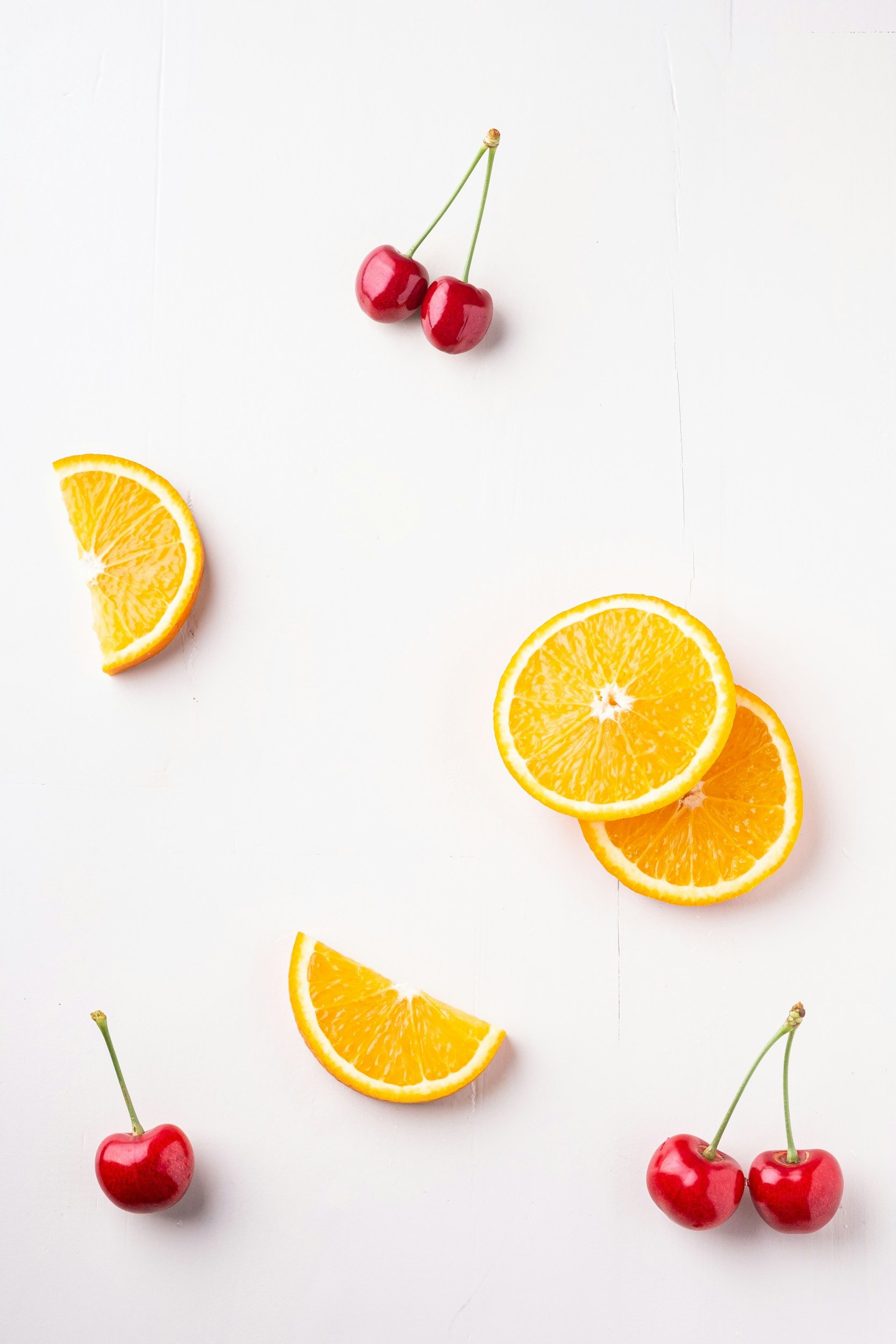 Three cherry stems and cherry halves, and four orange slices arranged on a white surface.