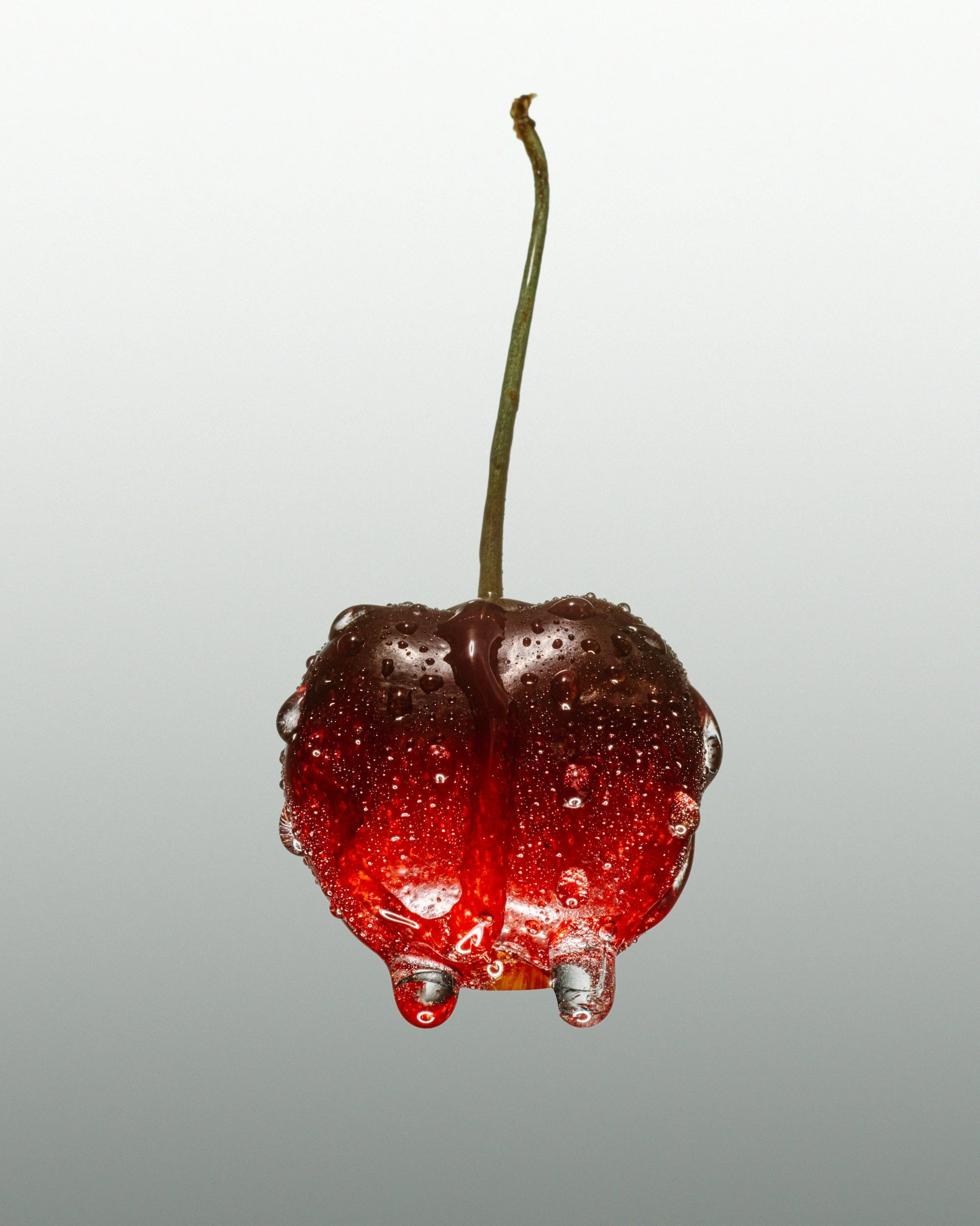 A cherry with water droplets on it, suspended upside down, clearly visible against a plain background.
